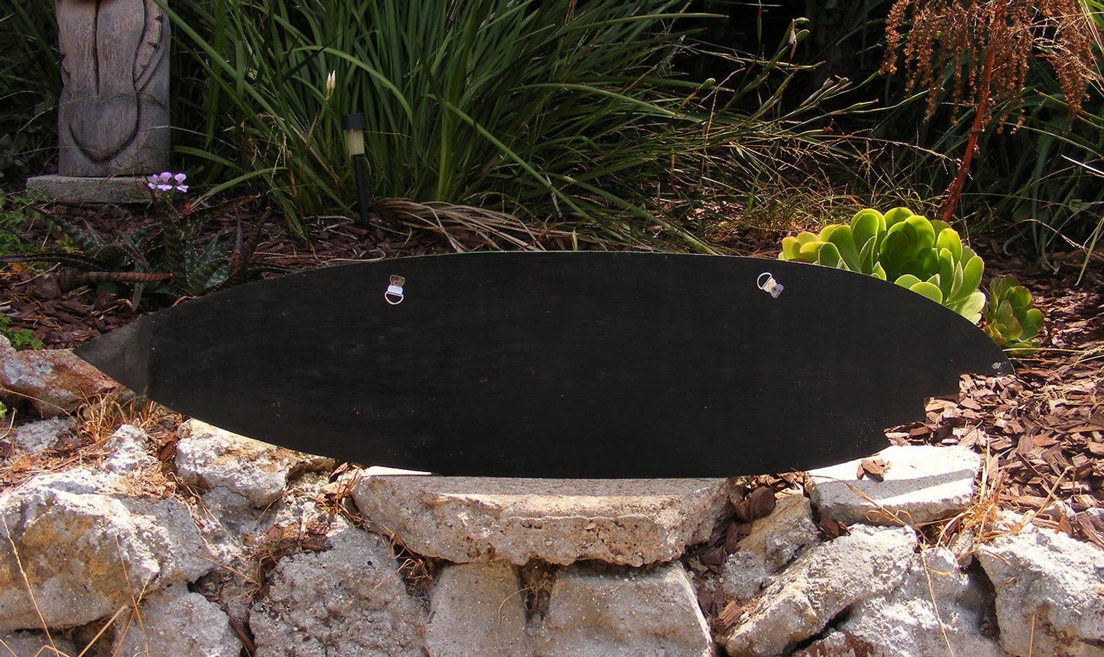 black oval board with two small metal handles resting on a stone garden wall among plants
