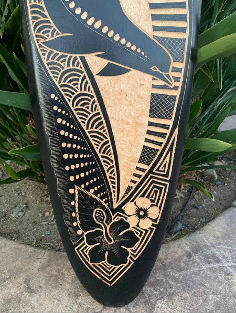 Black surfboard with beige wood-engraved hibiscus flower and geometric patterns