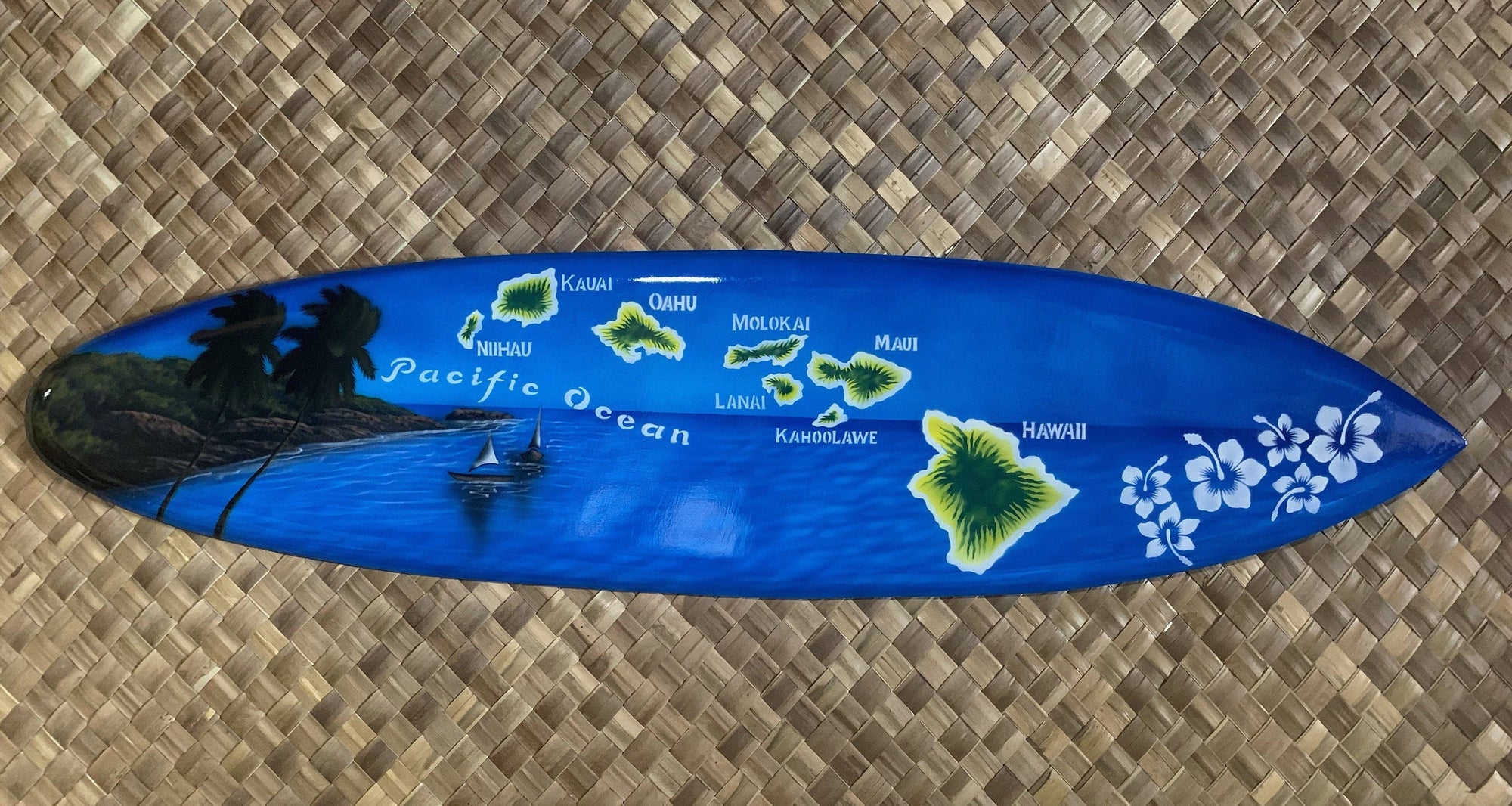Blue surfboard with a Hawaii island map, palm trees, and white hibiscus flowers.
