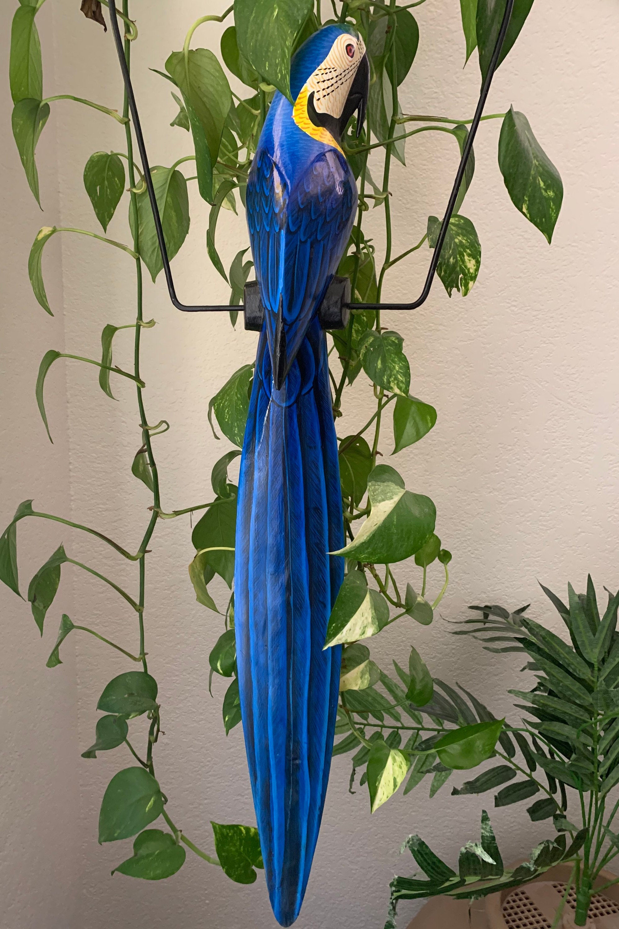 Blue macaw parrot sculpture hanging among green houseplants