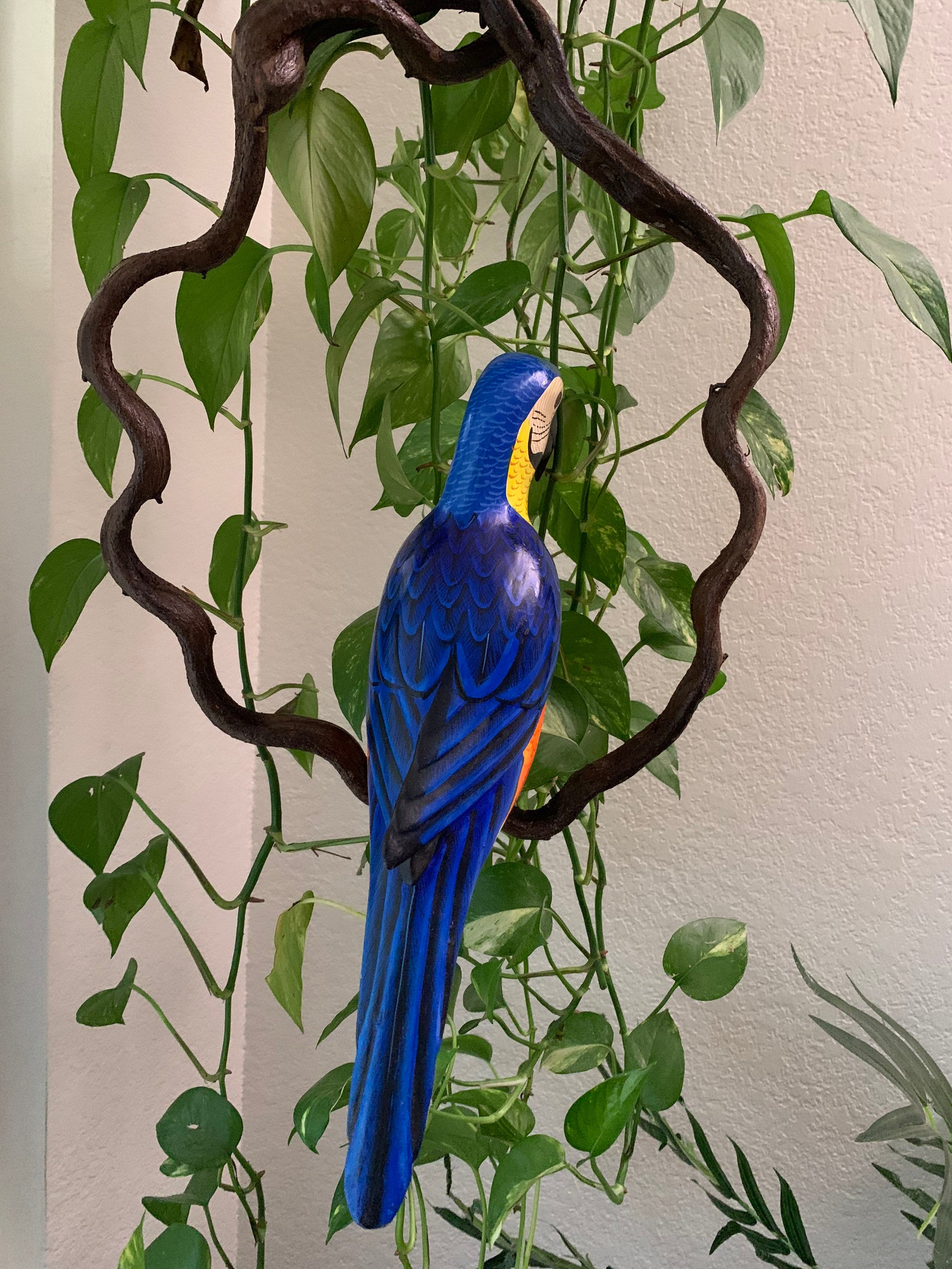 Blue macaw sculpture surrounded by green indoor plants and twisting branches.