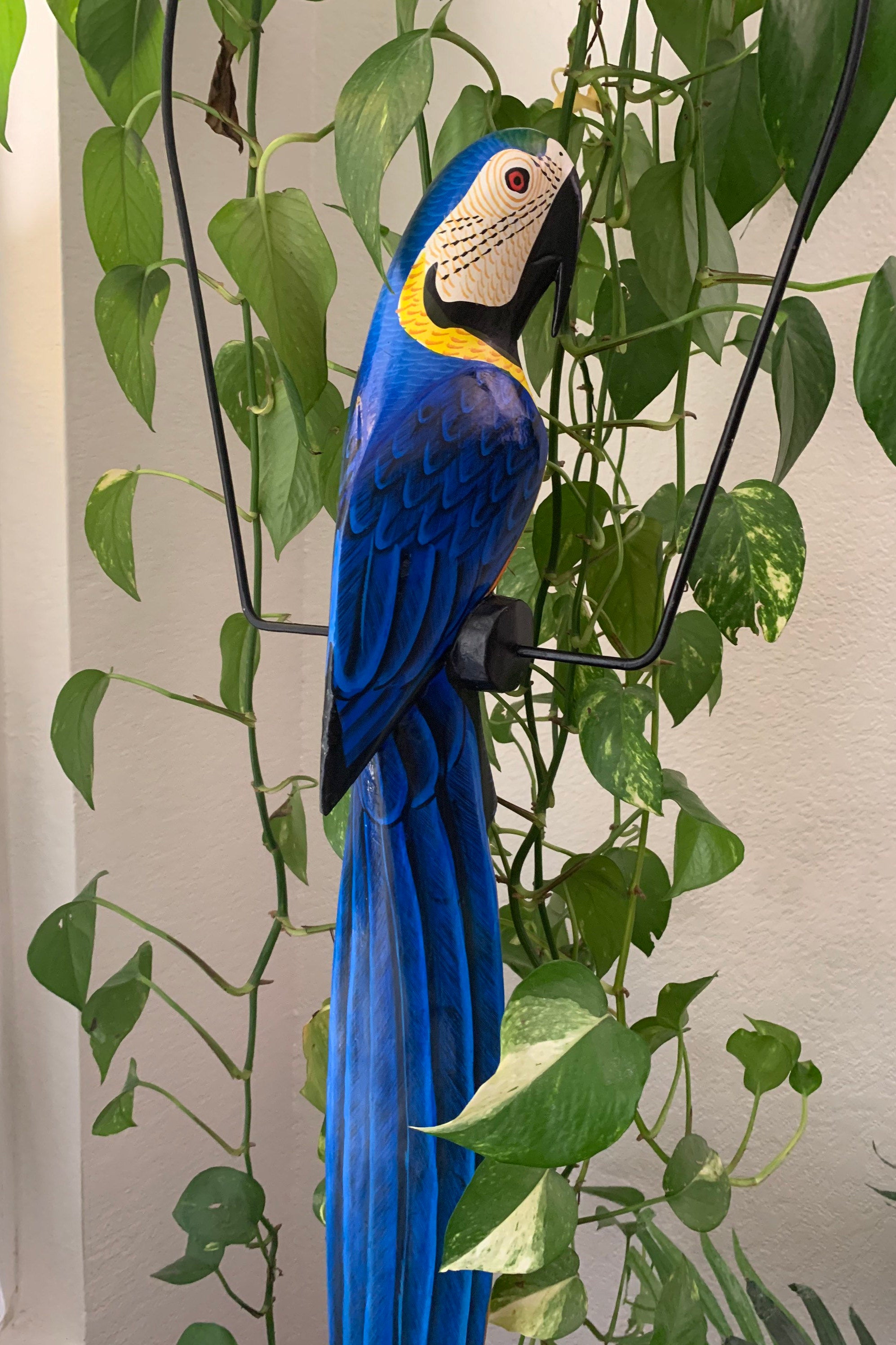 Bright blue macaw statue perched among green leafy vines