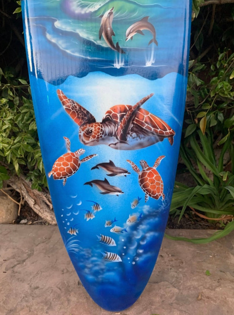 Blue surfboard art featuring sea turtles swimming with small fish in an ocean scene