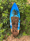 blue surfboard featuring a tiki face and a palm tree on a tropical beach