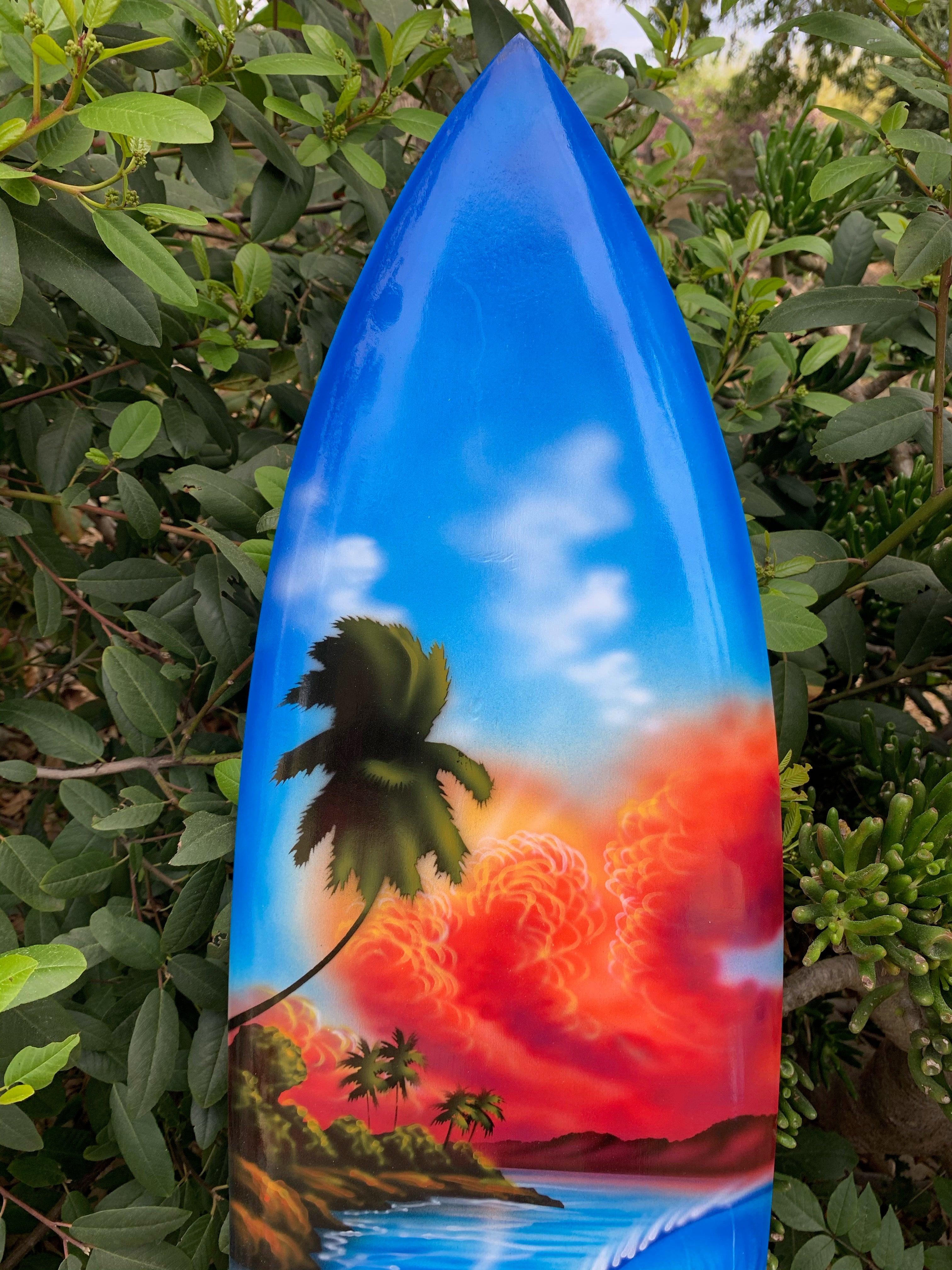 Blue surfboard with tropical sunset, palm trees, and ocean shoreline