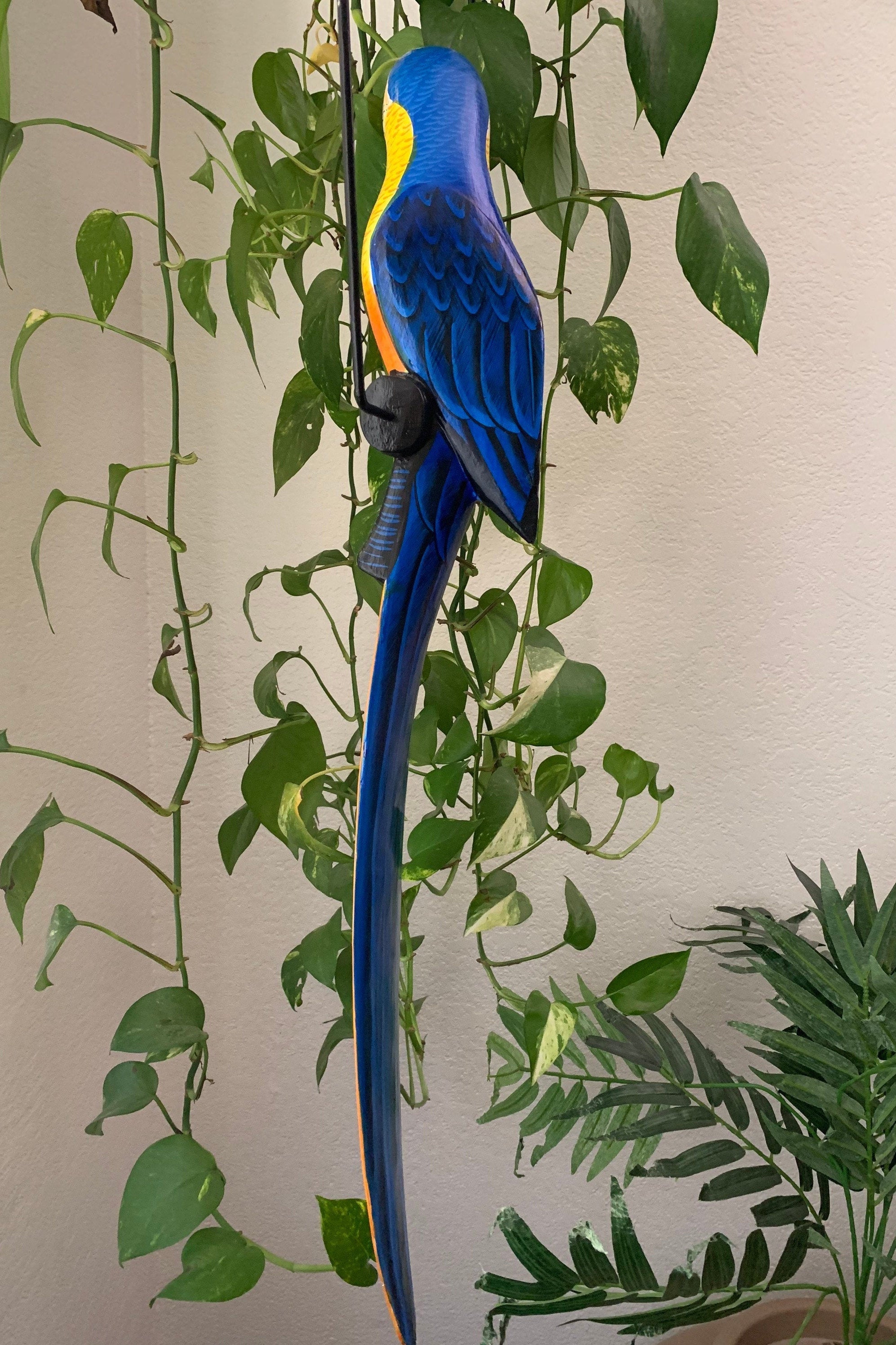 Blue-and-yellow macaw sculpture perched among green plants