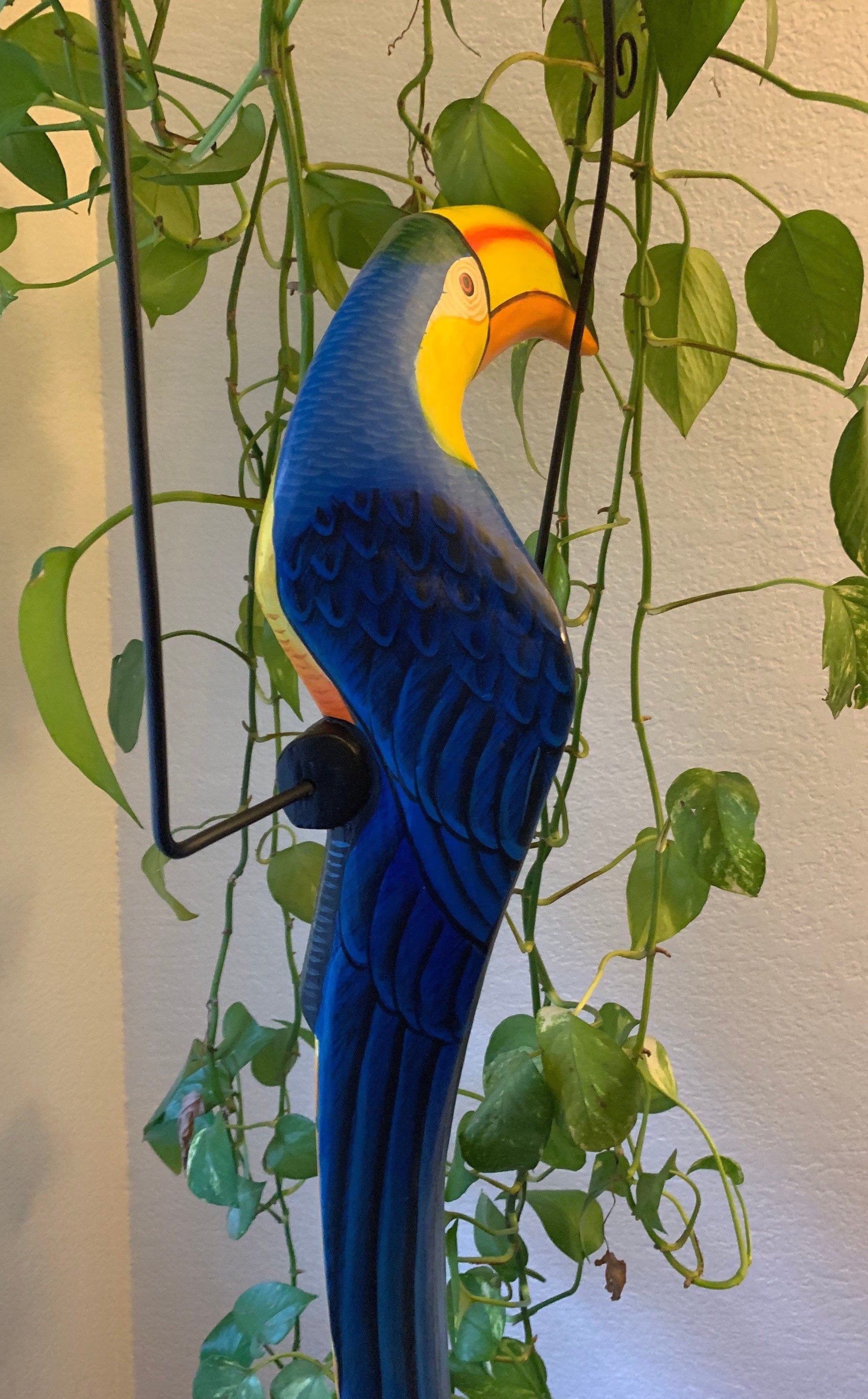 Blue-yellow macaw sculpture among hanging green plants