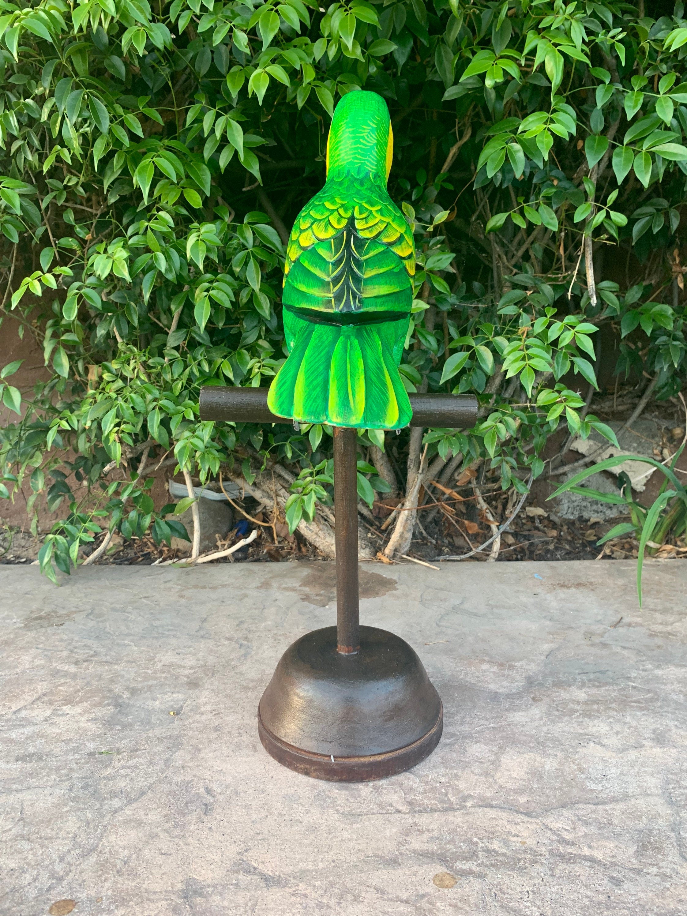 bright green parrot statue perched on a metal stand with leafy shrubs in the background