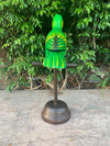 bright green parrot statue perched on a metal stand with leafy shrubs in the background