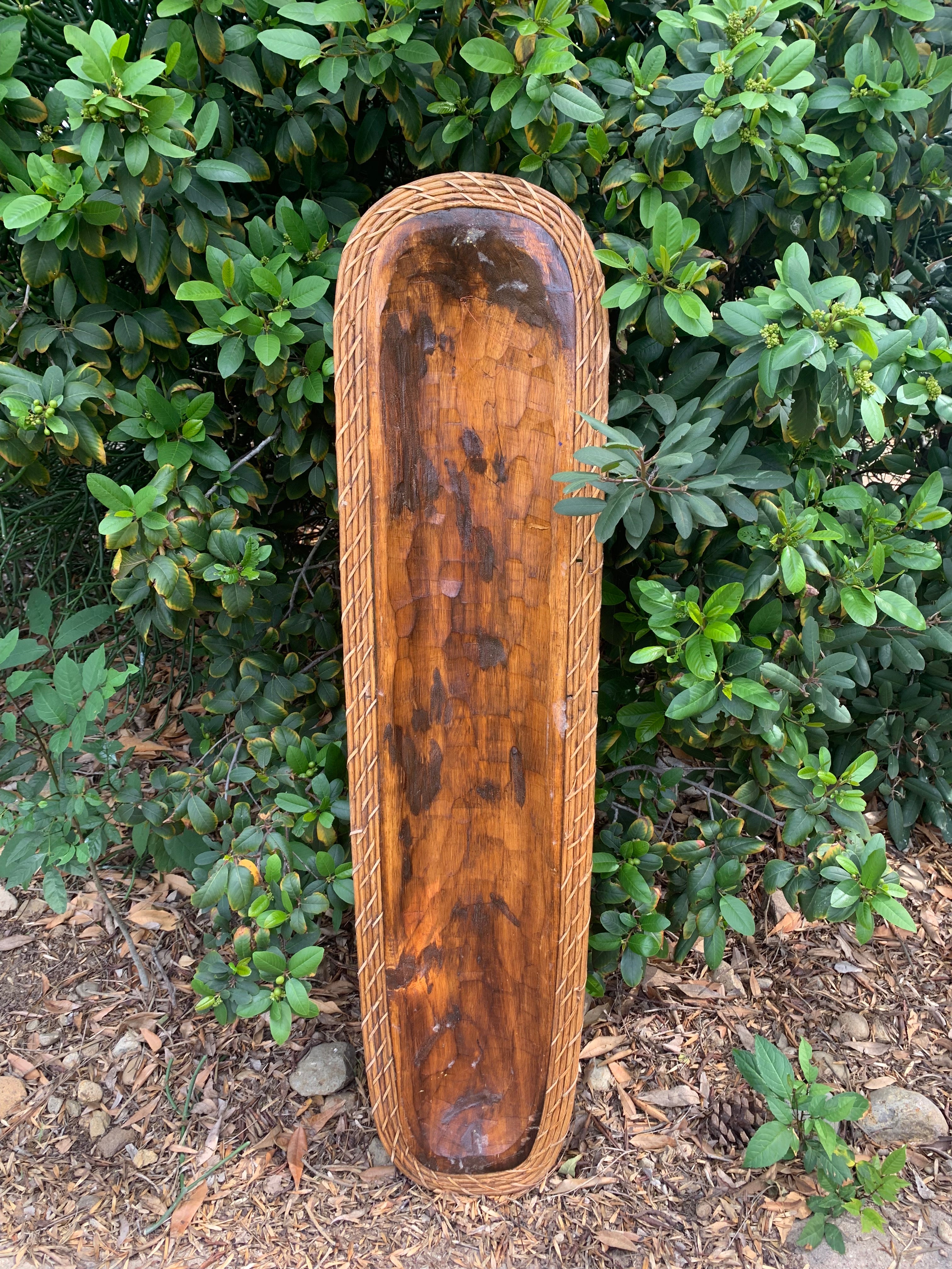 Canoe-shaped wooden tray with braided rope border outdoors.