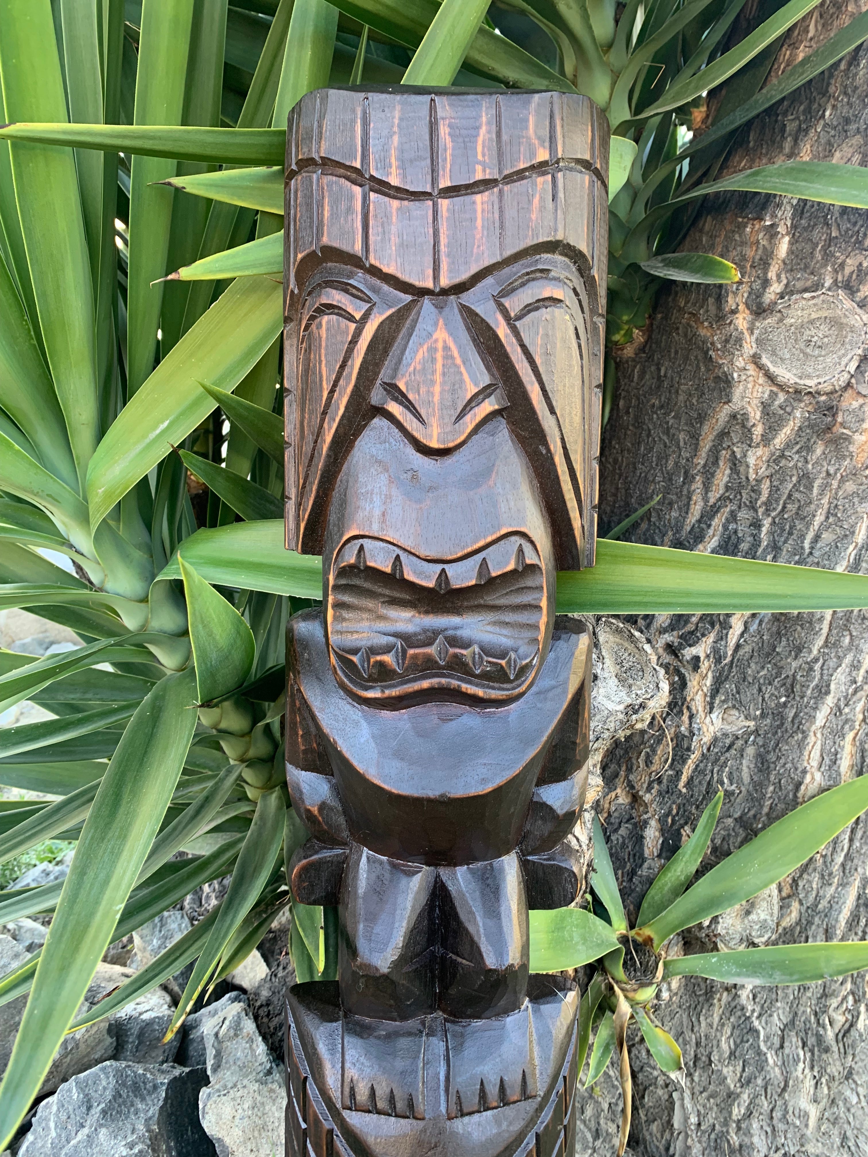 Carved wooden tiki totem statue outdoors among greenery.