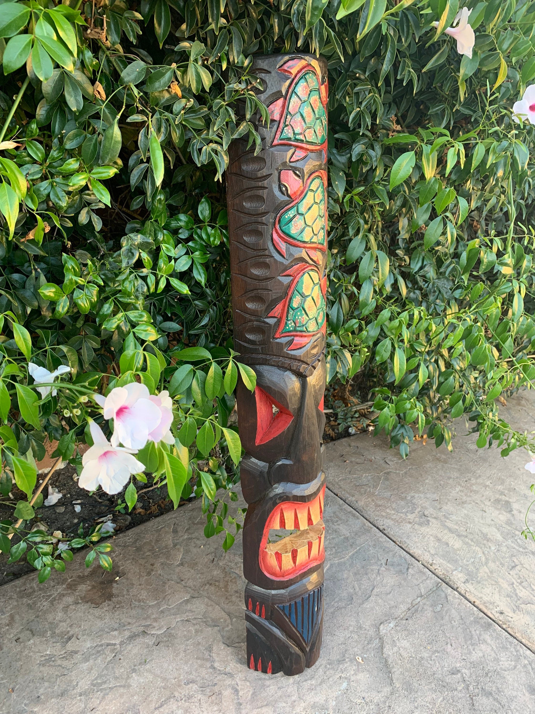Wooden totem pole with colorful turtle designs beside a leafy hedge