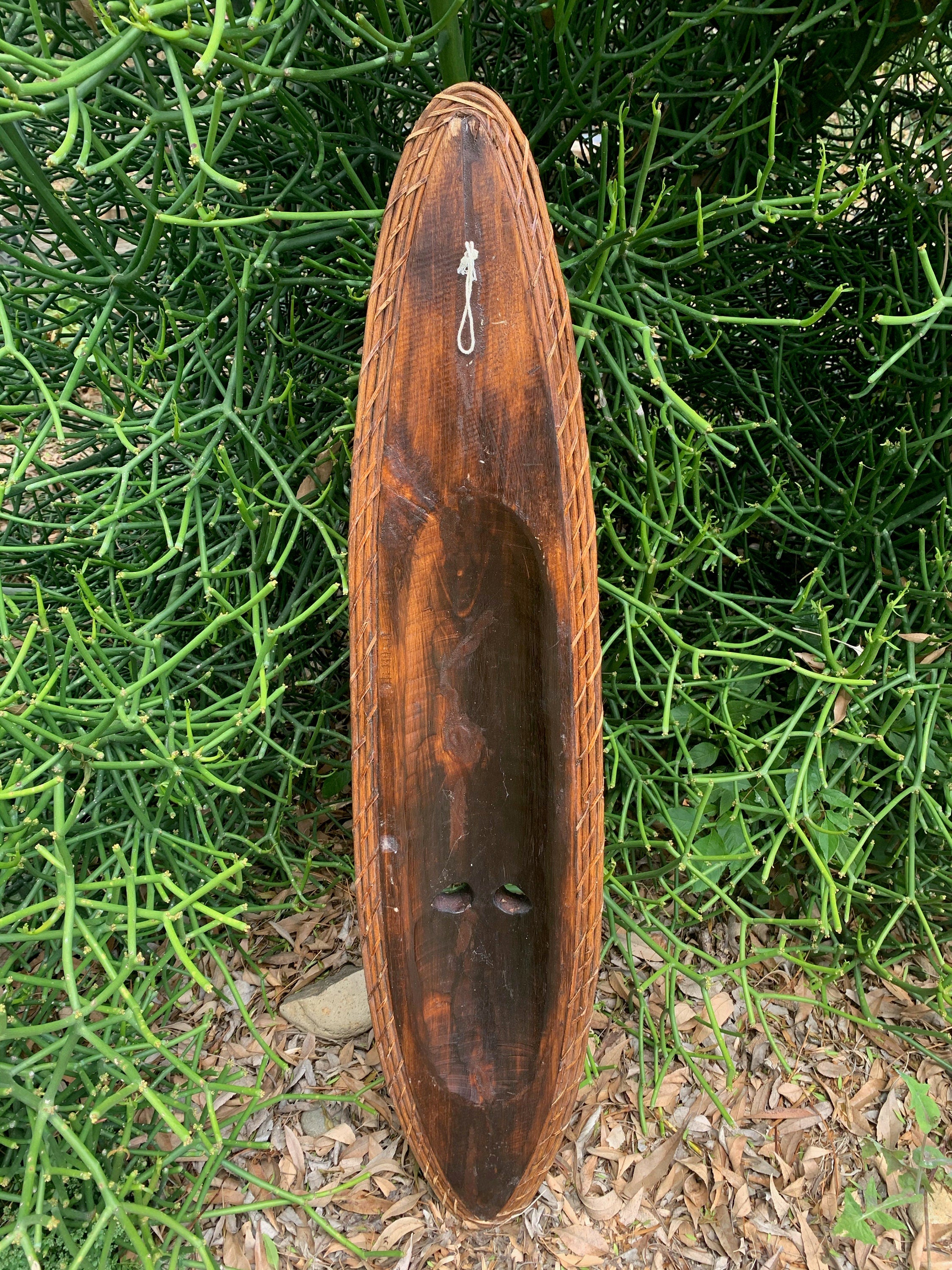 carved wooden canoe-shaped trough with rope border leaning against green shrub