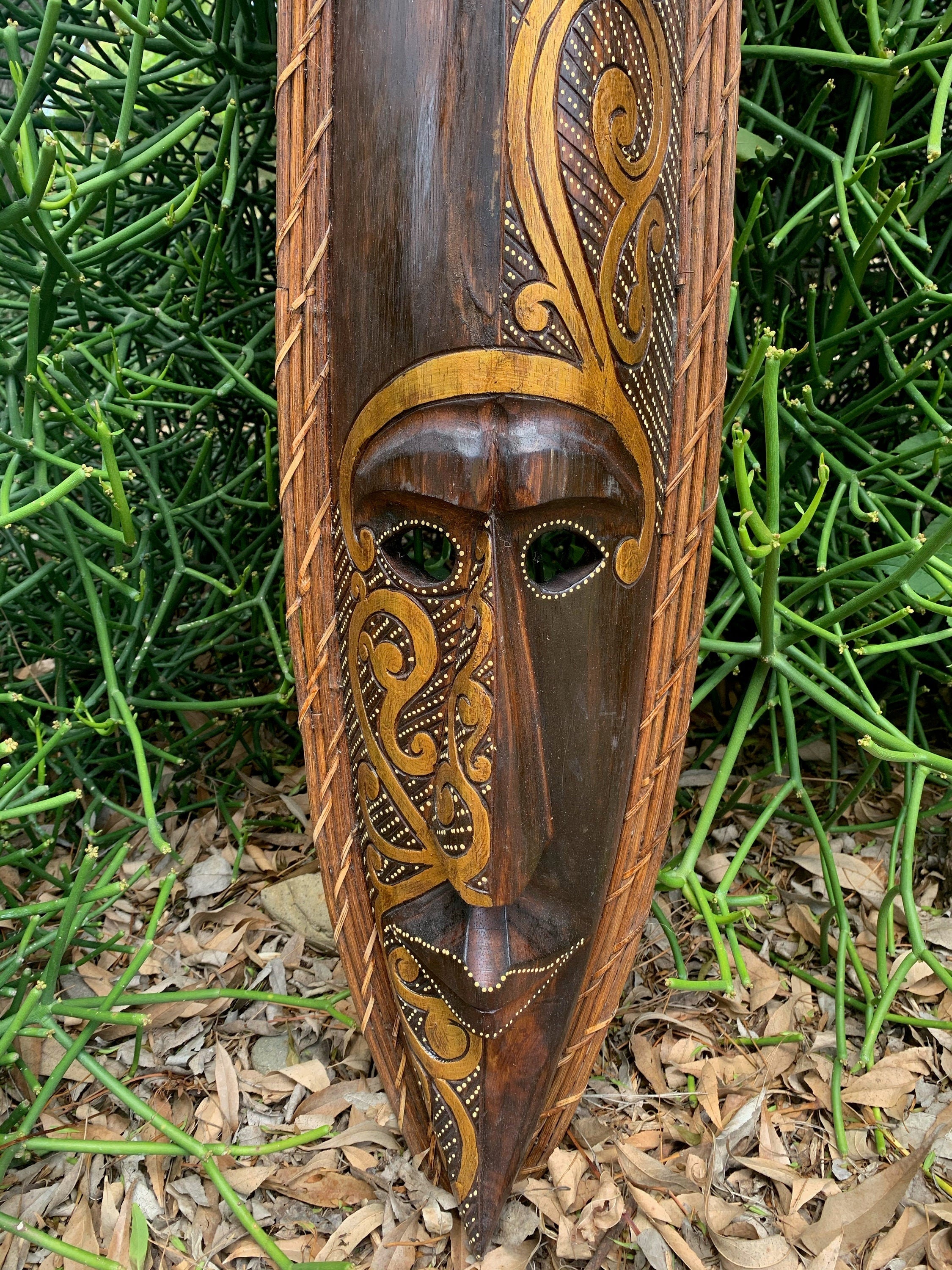 Carved wooden mask with gold swirls on a wooden pole against green foliage