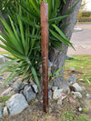 Carved wooden pole leaning against a tree beside a spiky green-leaved plant and rocks