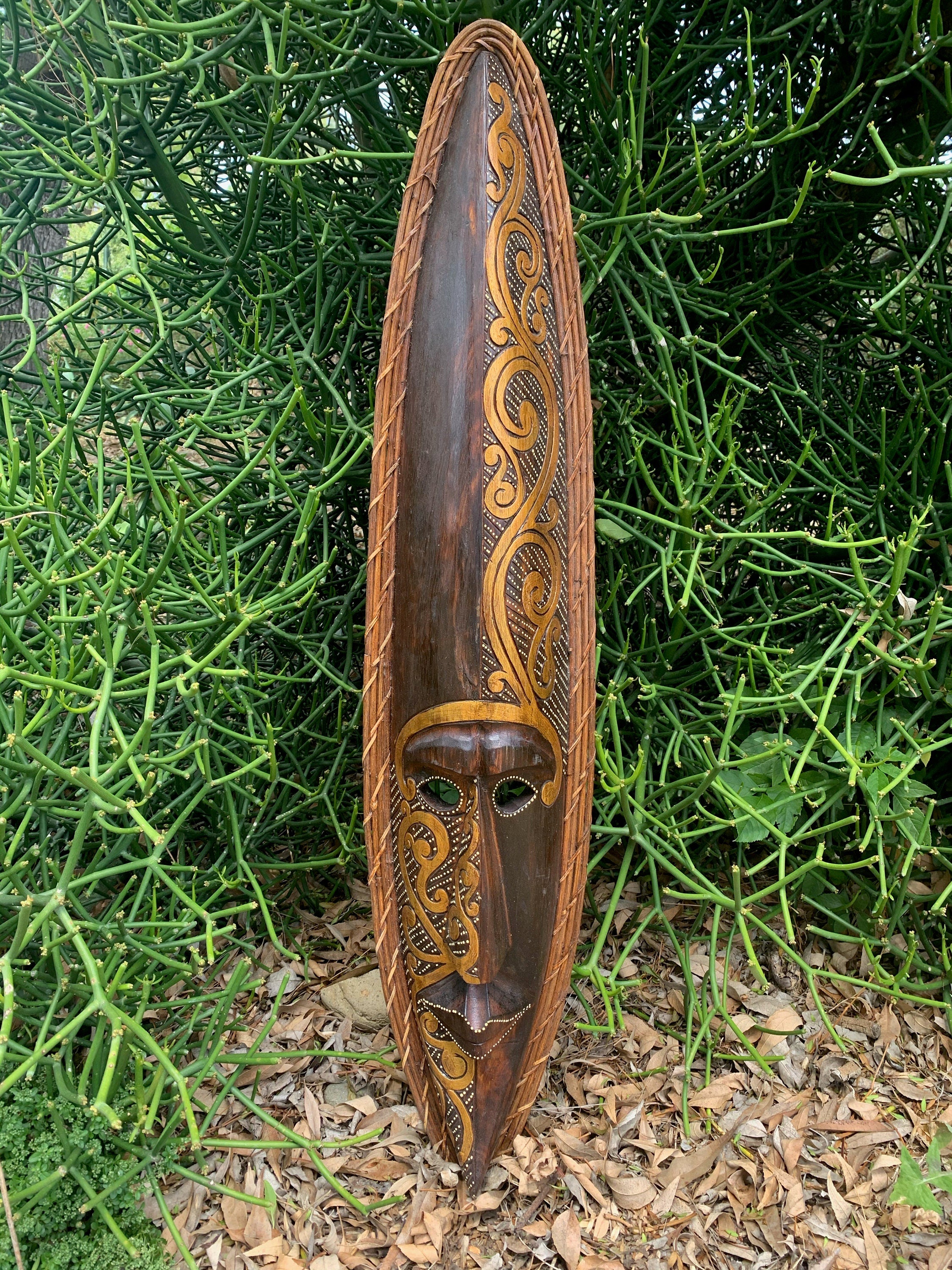 Carved wooden shield featuring a masked-face and ornate gold swirls against a green background.