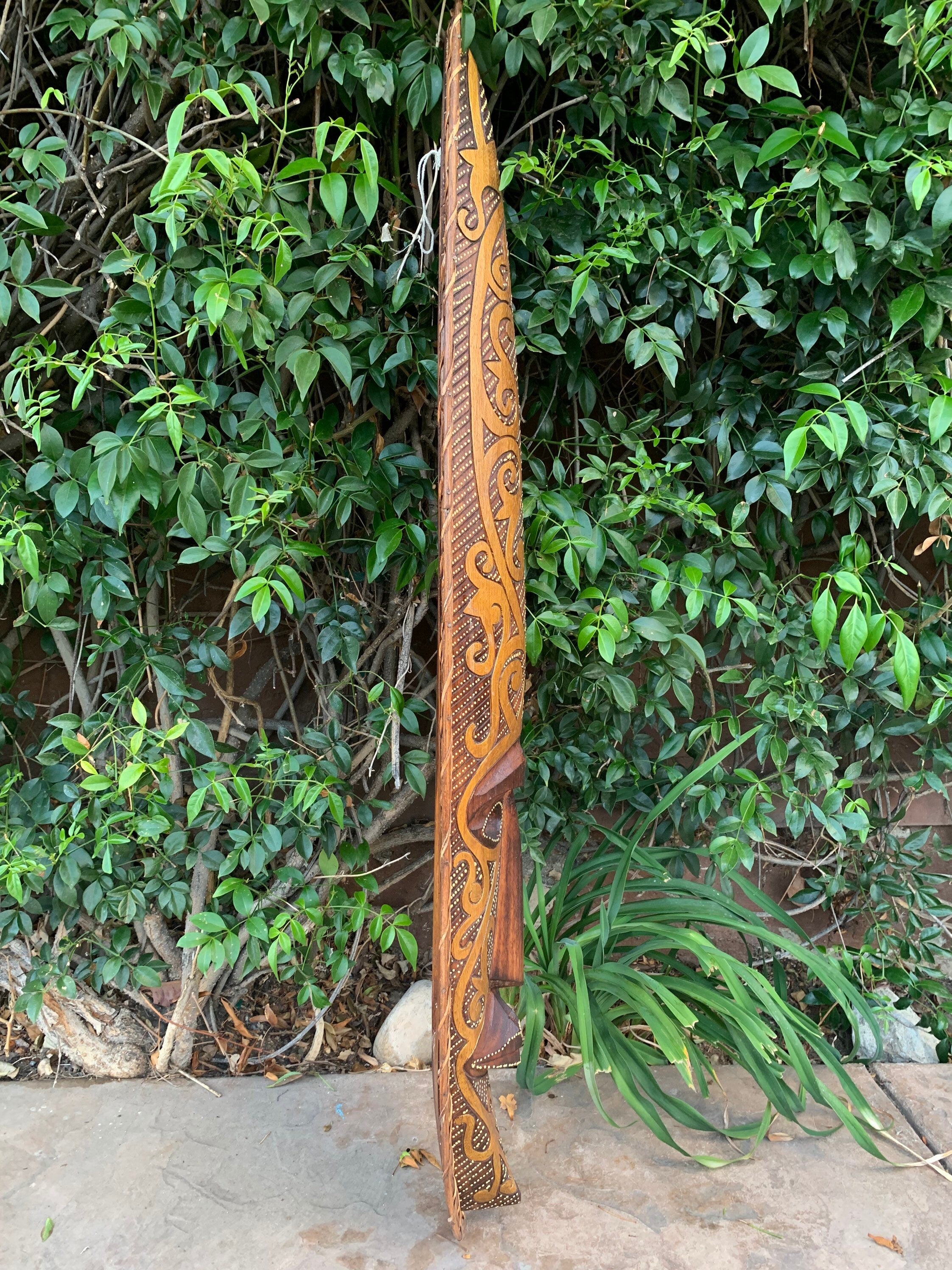Carved wooden staff with swirling tiki patterns leaning against green foliage.
