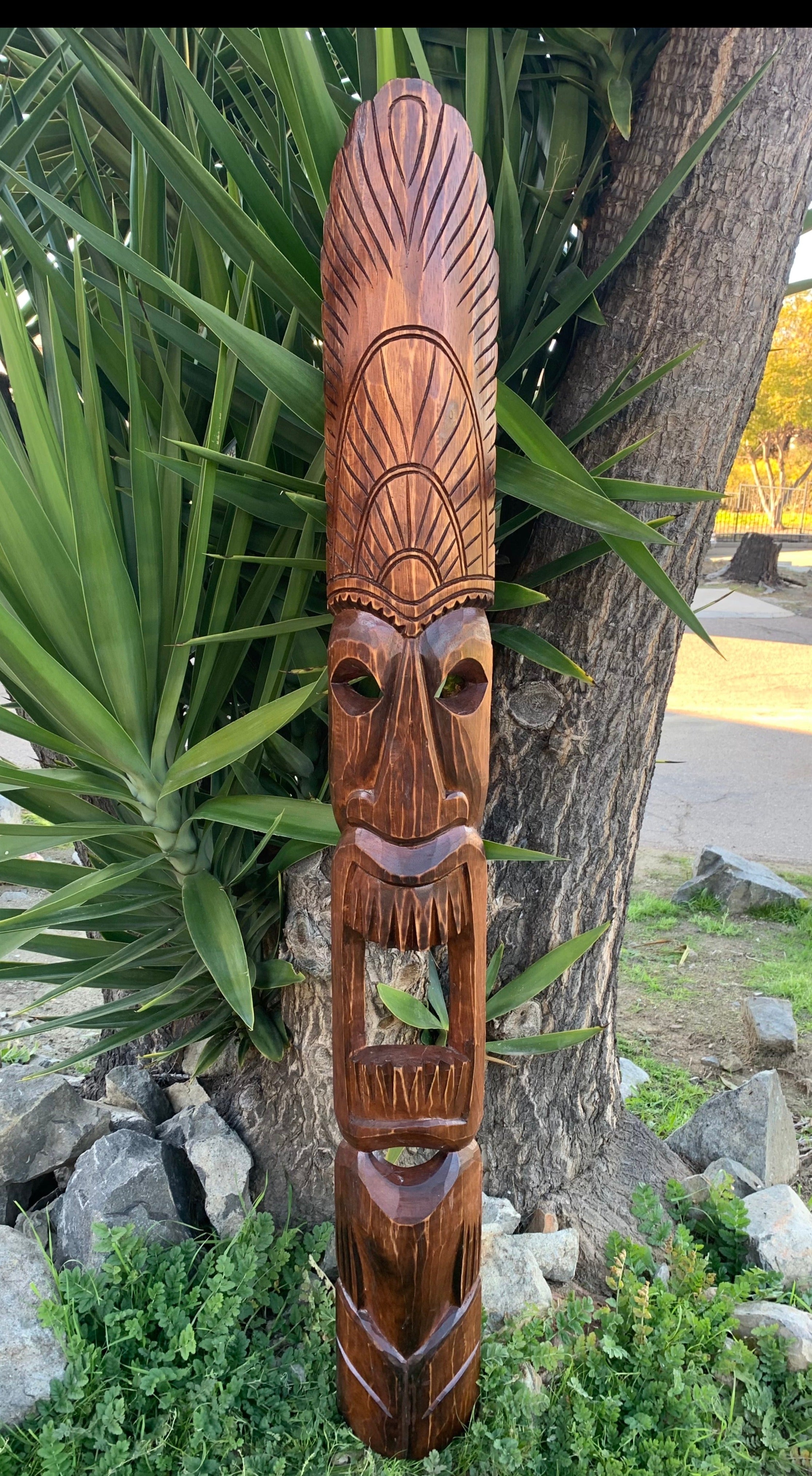 Wooden tiki mask with tall carved headdress in a garden