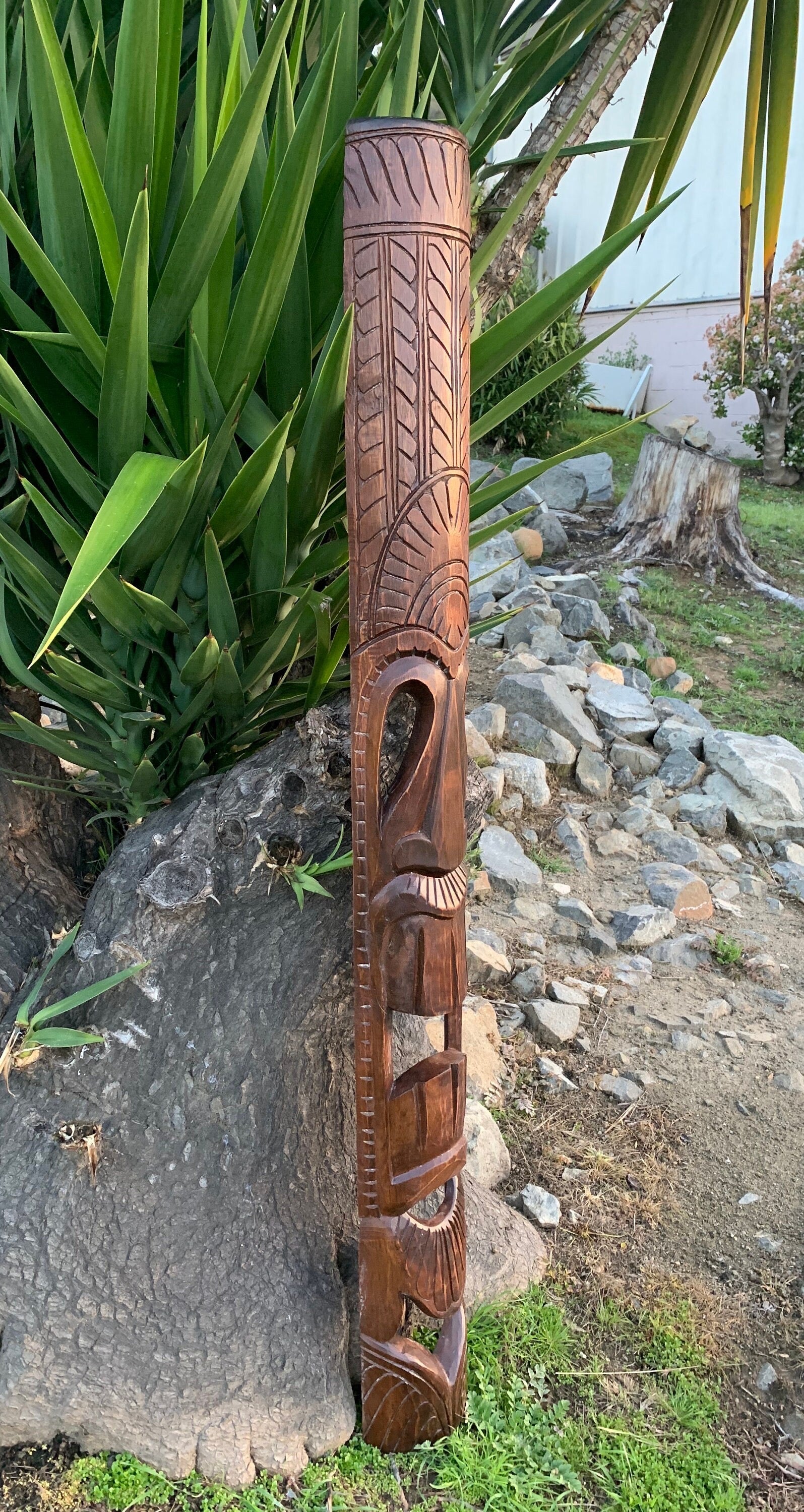 Tall carved wooden tiki pole with geometric patterns in an outdoor garden among rocks