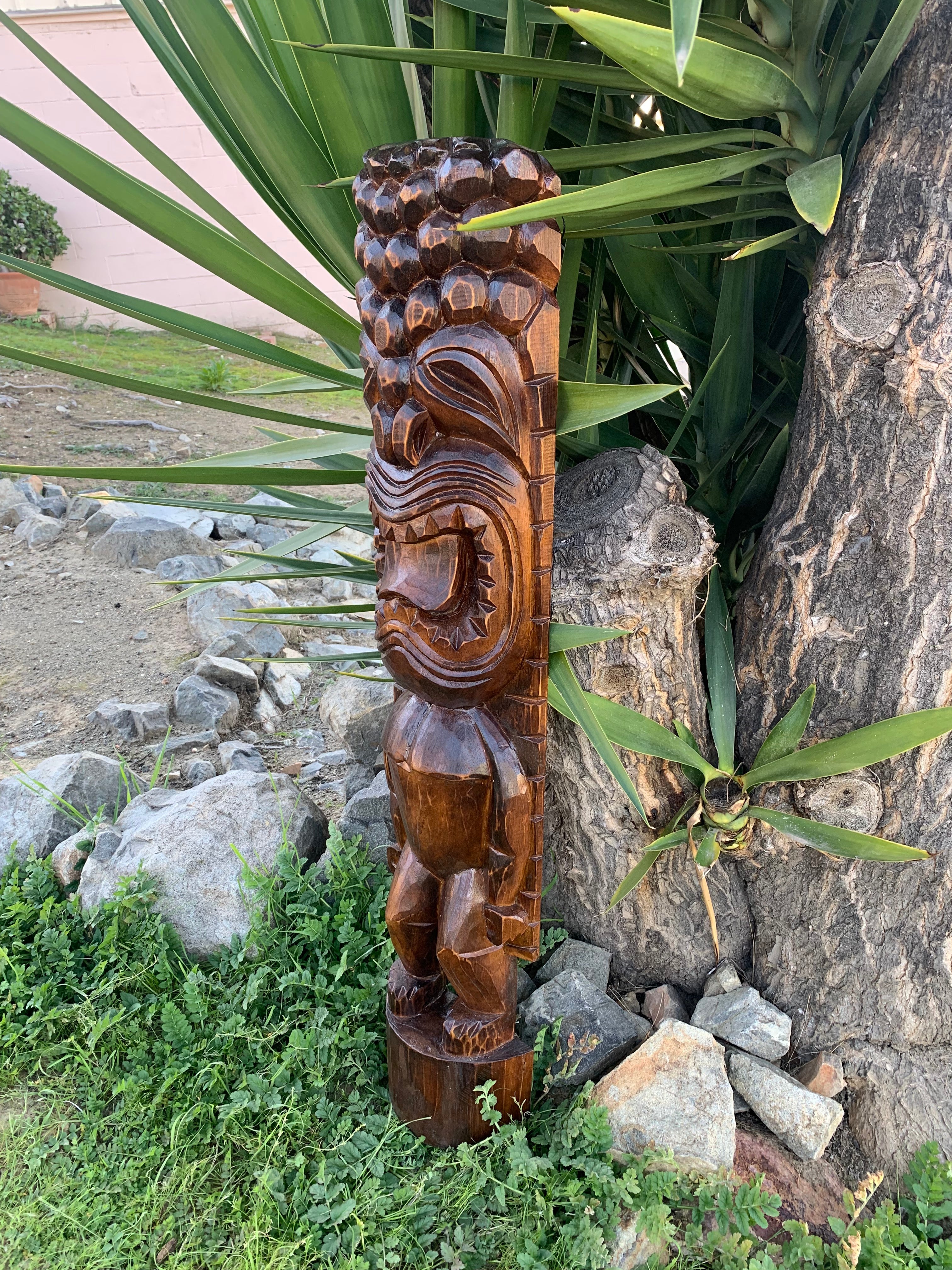 Carved wooden tiki statue outdoors beside a tree and rocks