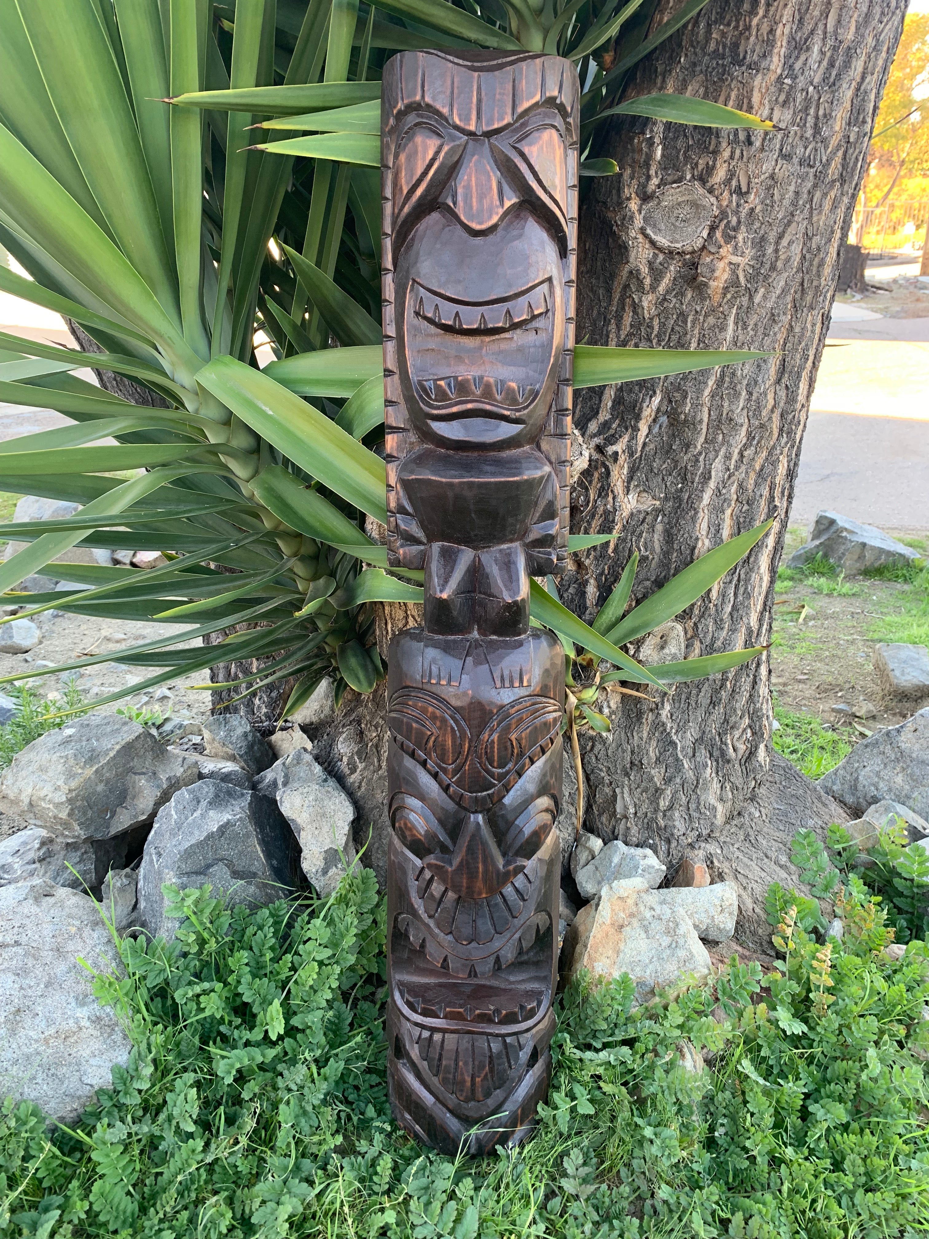 Carved wooden tiki totem pole with multiple faces outdoors