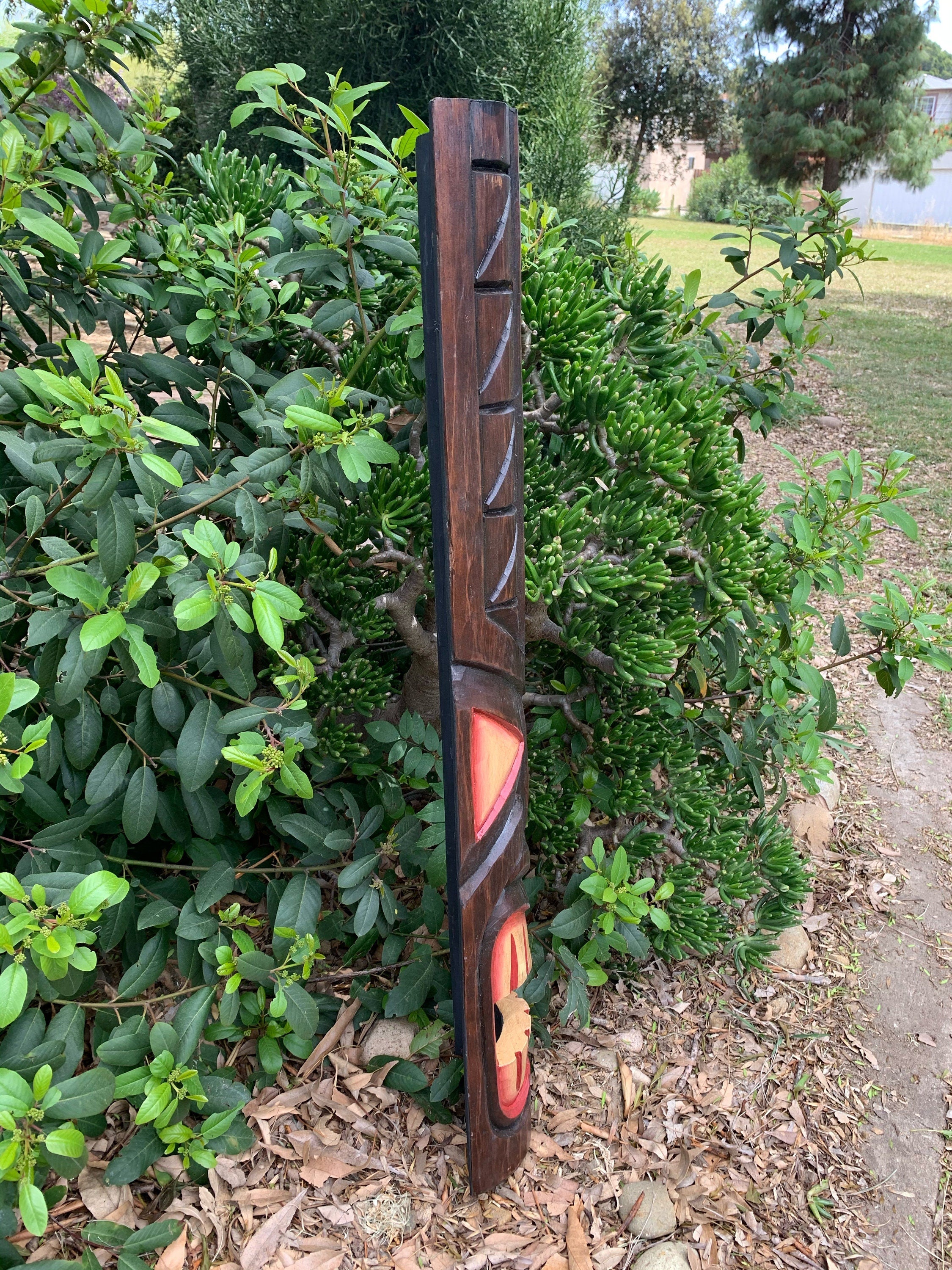 Tall carved wooden totem pole leaning against shrubs in a garden setting.