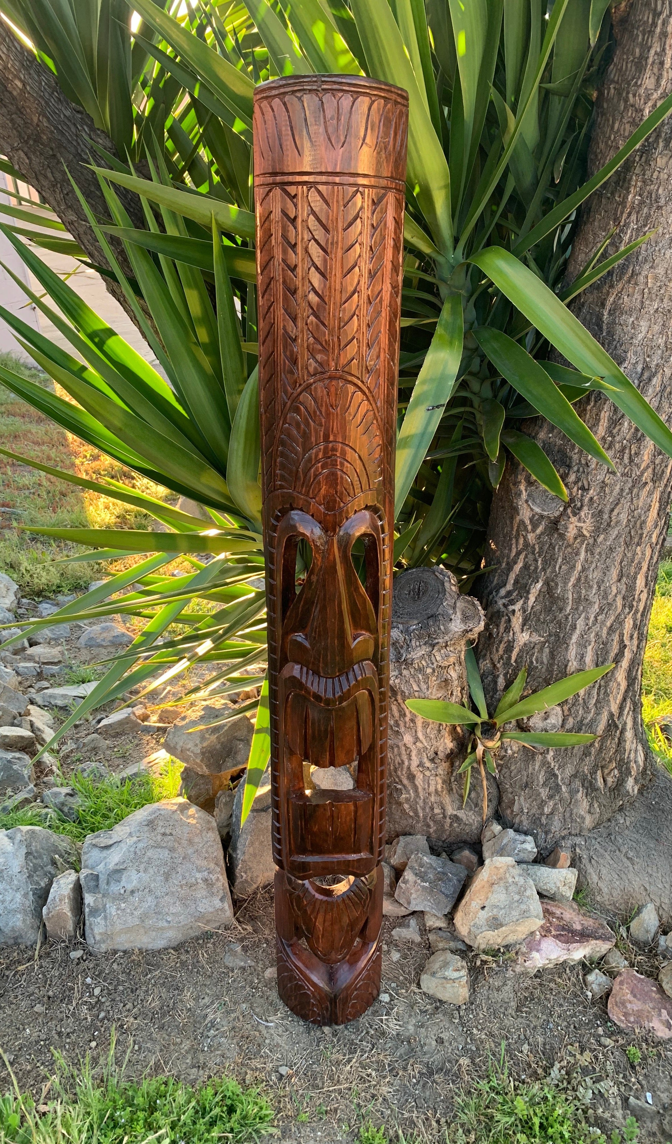 carved wooden totem pole with a facial mask design outdoors in a garden