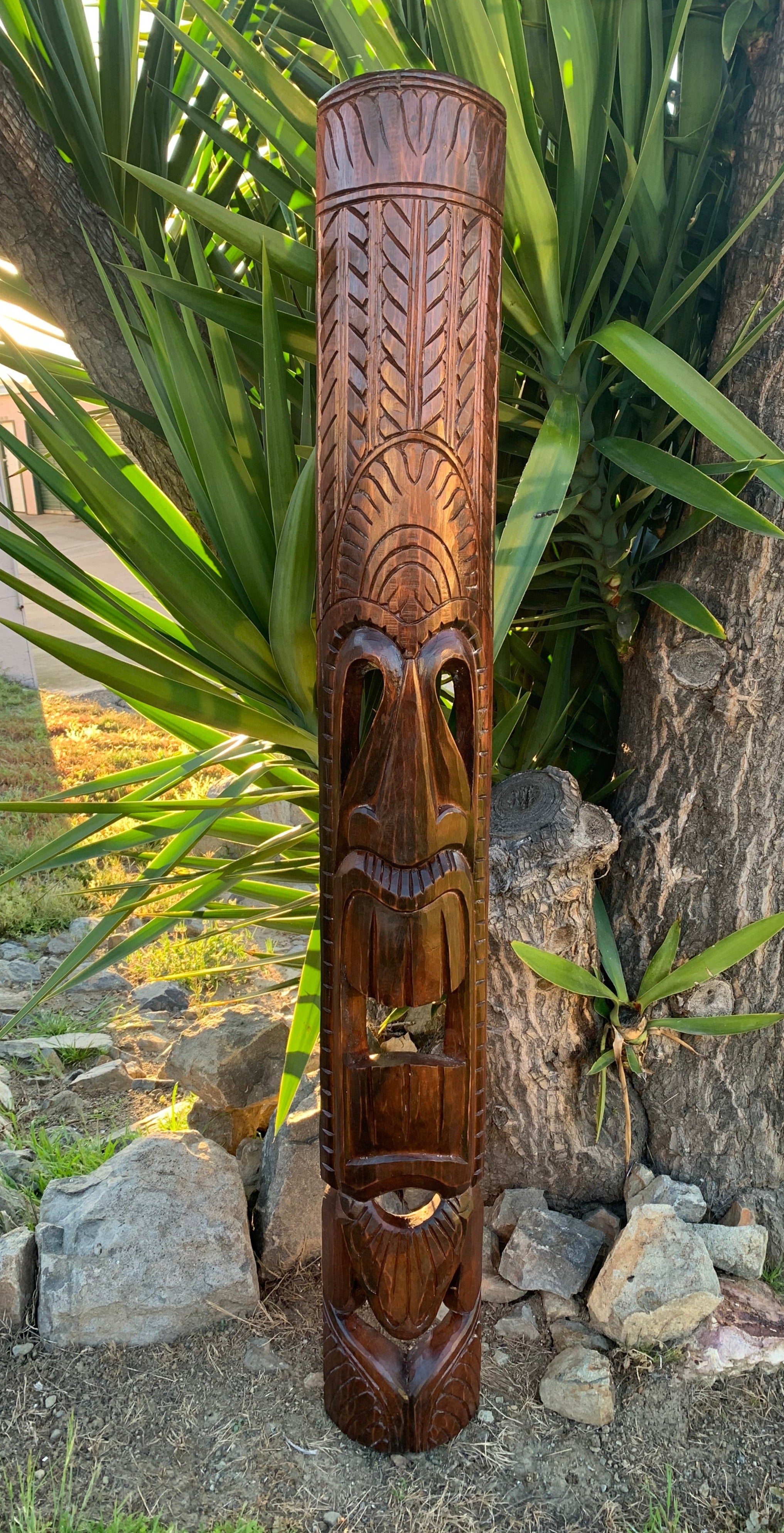tall carved wooden totem pole with intricate patterns in a garden setting