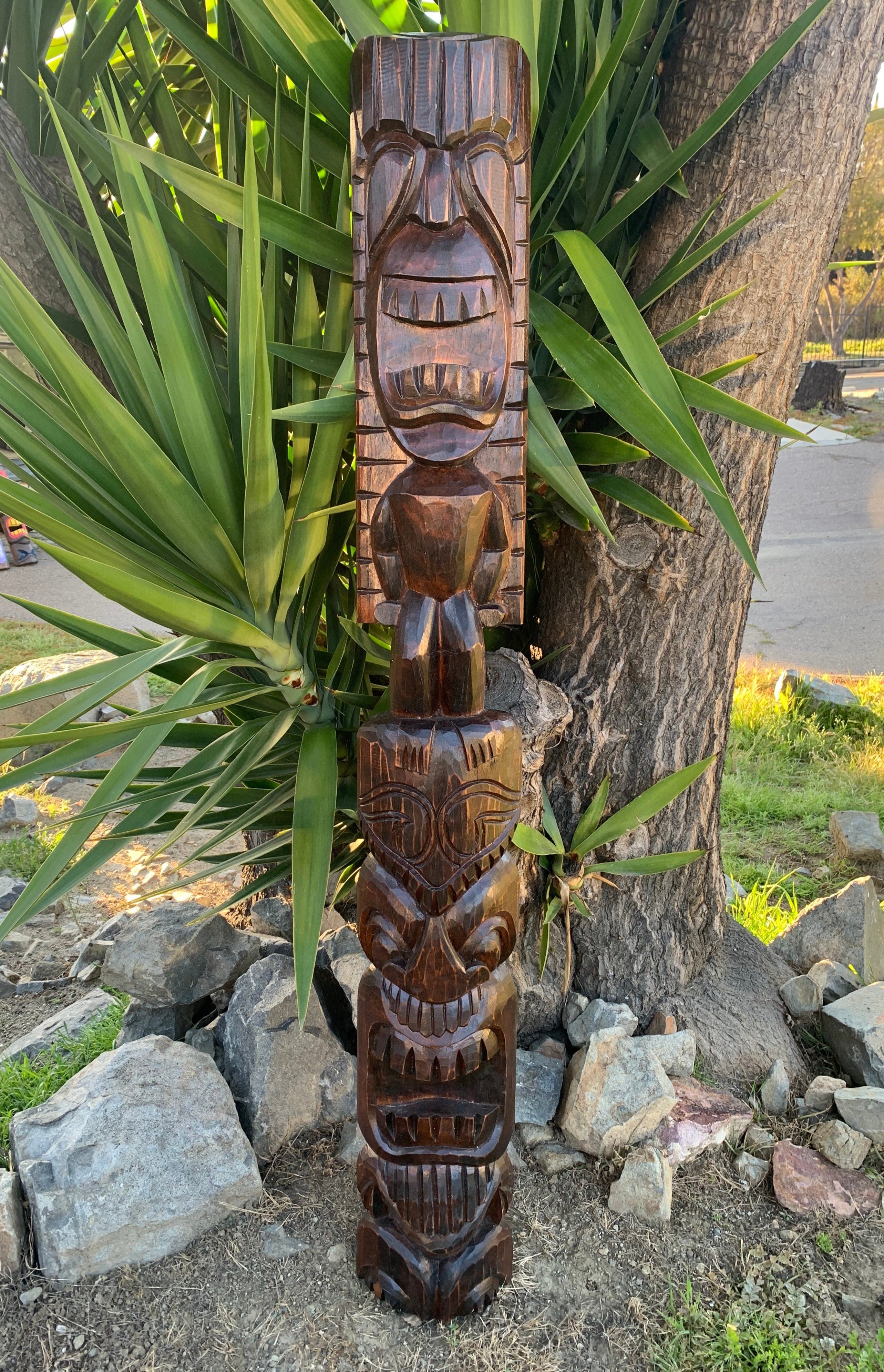 Carved wooden totem pole with stacked faces outdoors near a tree