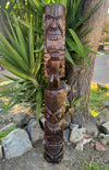 Carved wooden totem pole with stacked faces outdoors near a tree