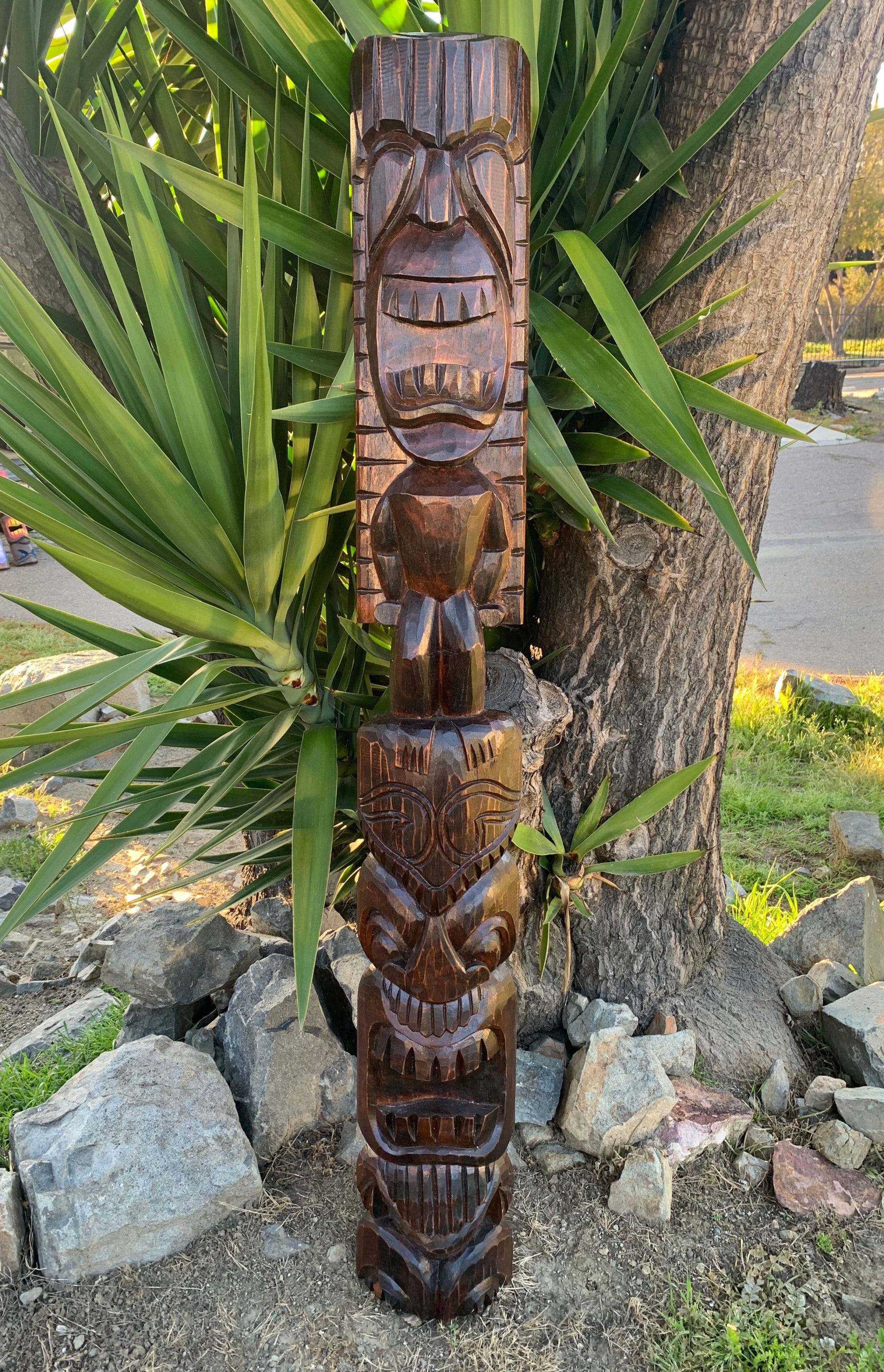 Carved wooden totem pole with stacked faces outdoors near a tree