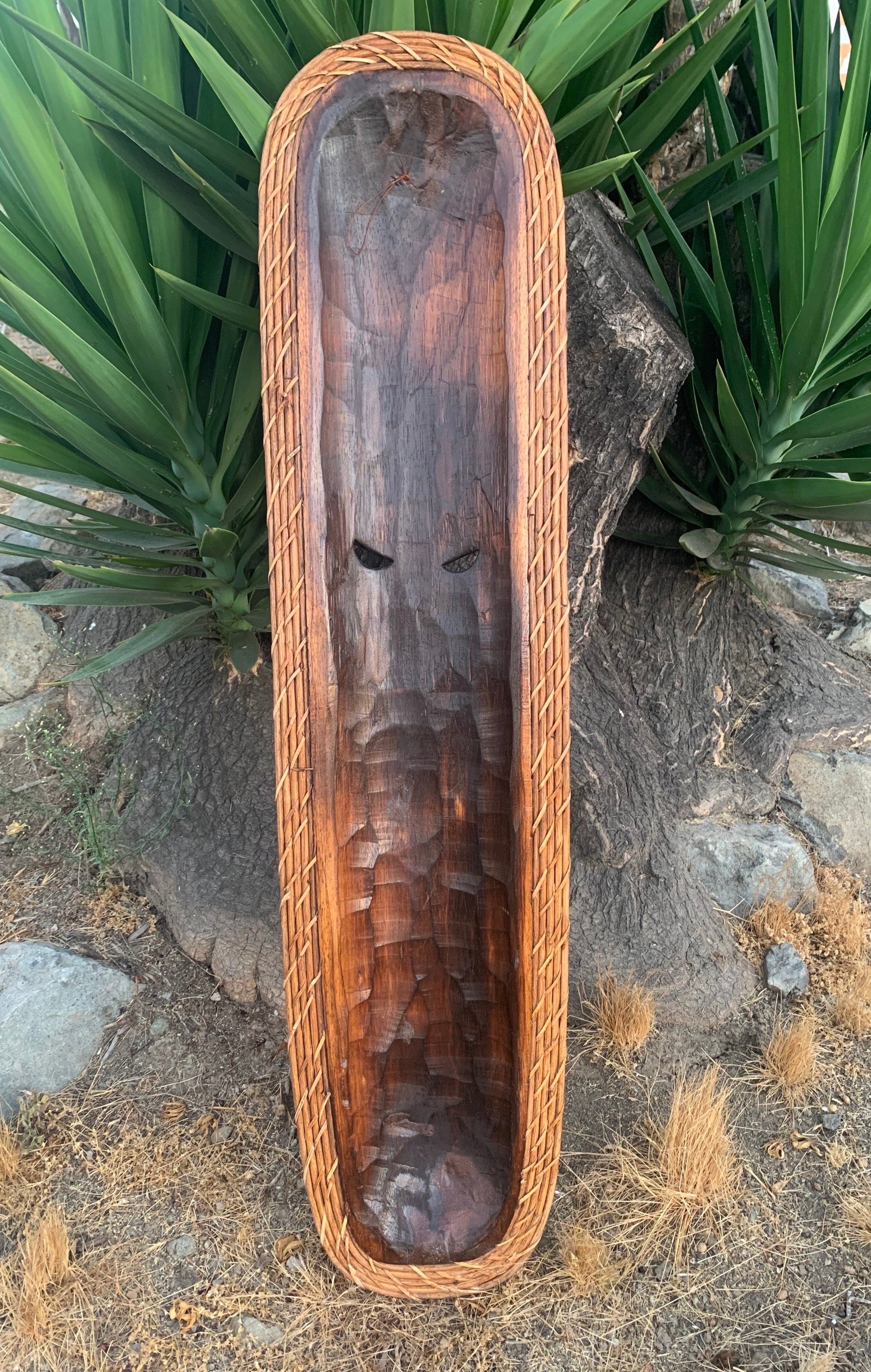 long carved wooden trough with braided border placed outdoors beside agave plants