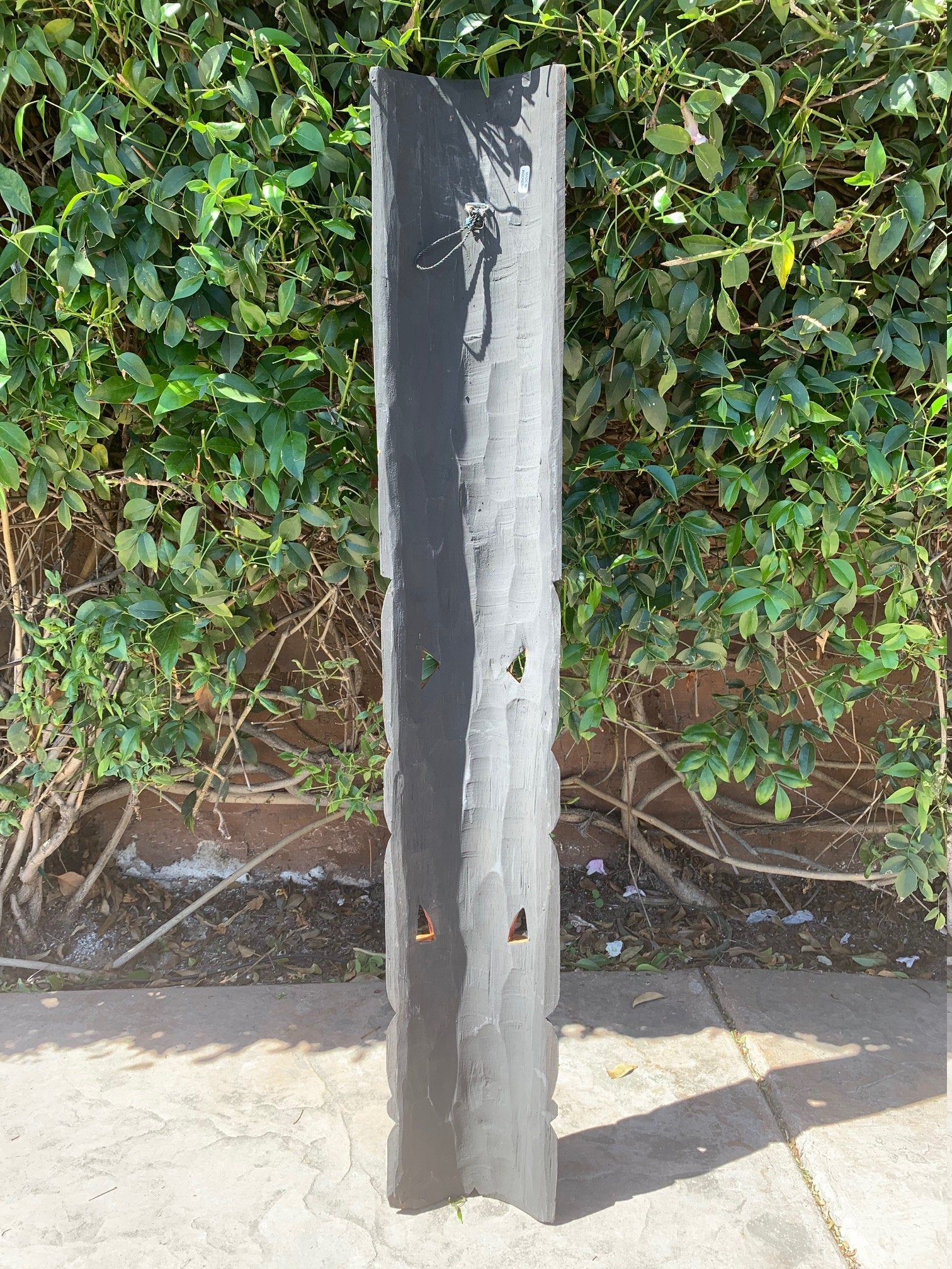 Charred wooden post lantern with triangular openings lit from inside in a garden setting