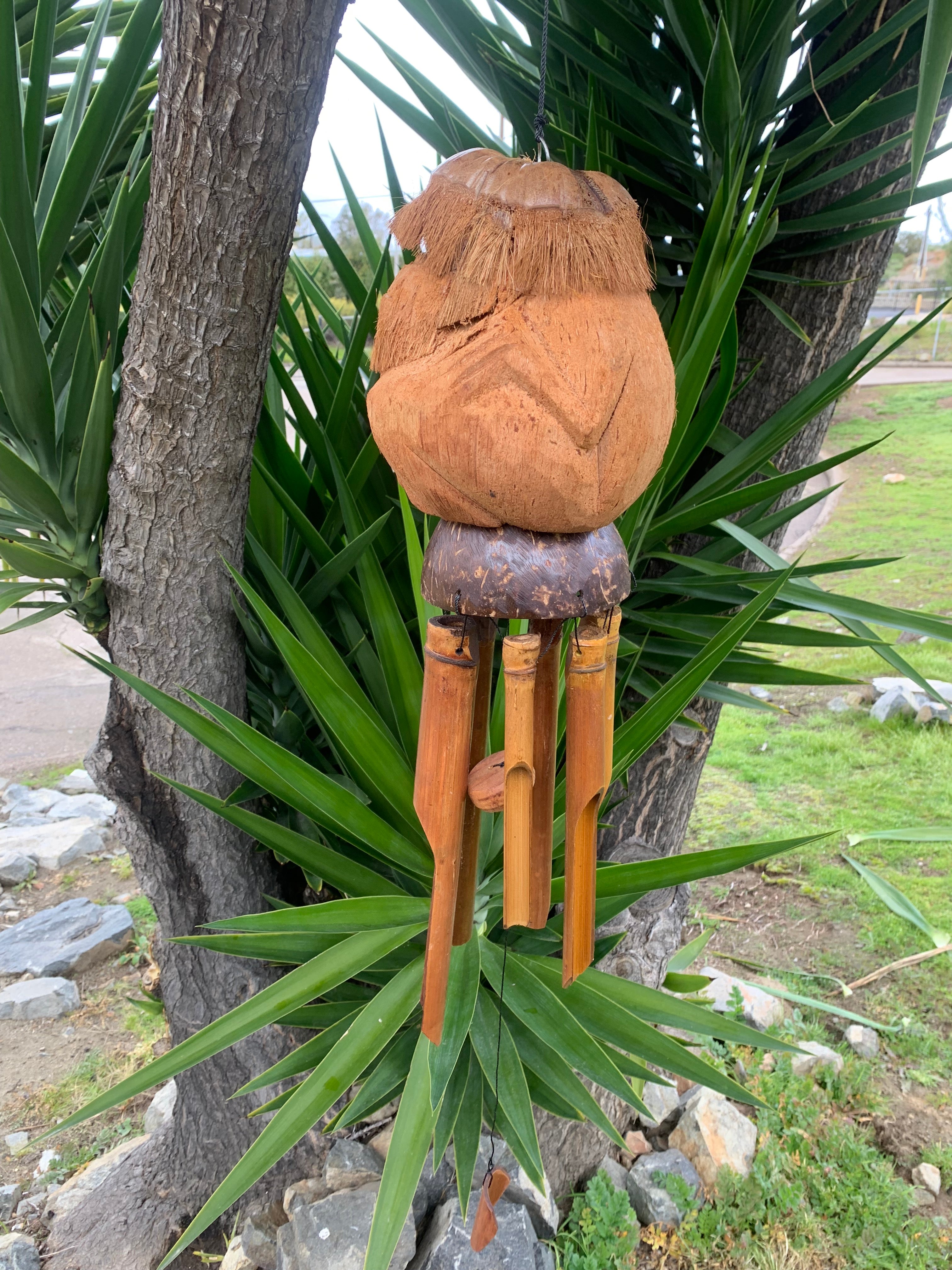 wooden tiki wind chime with bamboo tubes hanging from a coconut-top on a tree