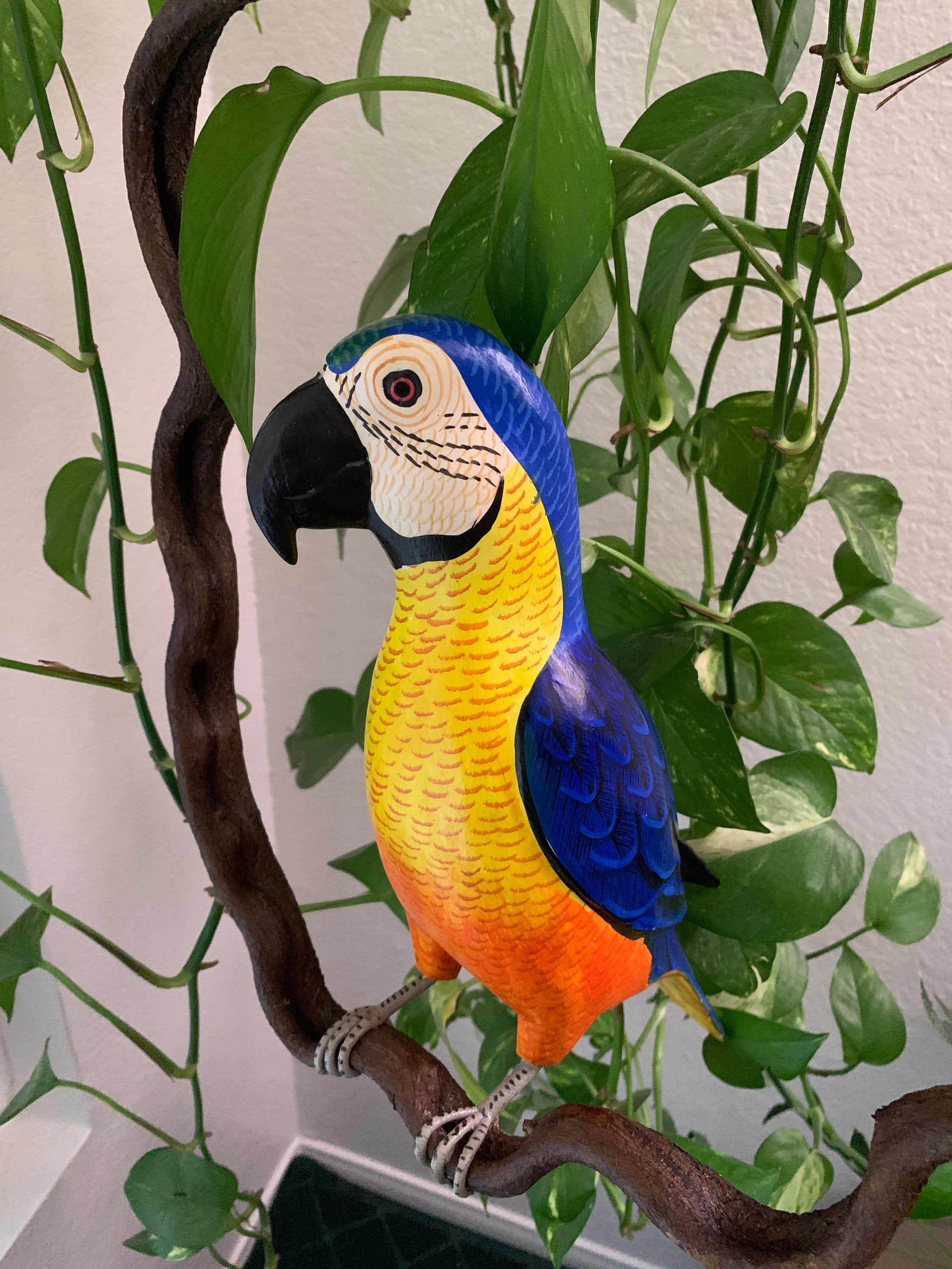Colorful blue-and-yellow macaw statue perched on a branch among green leaves
