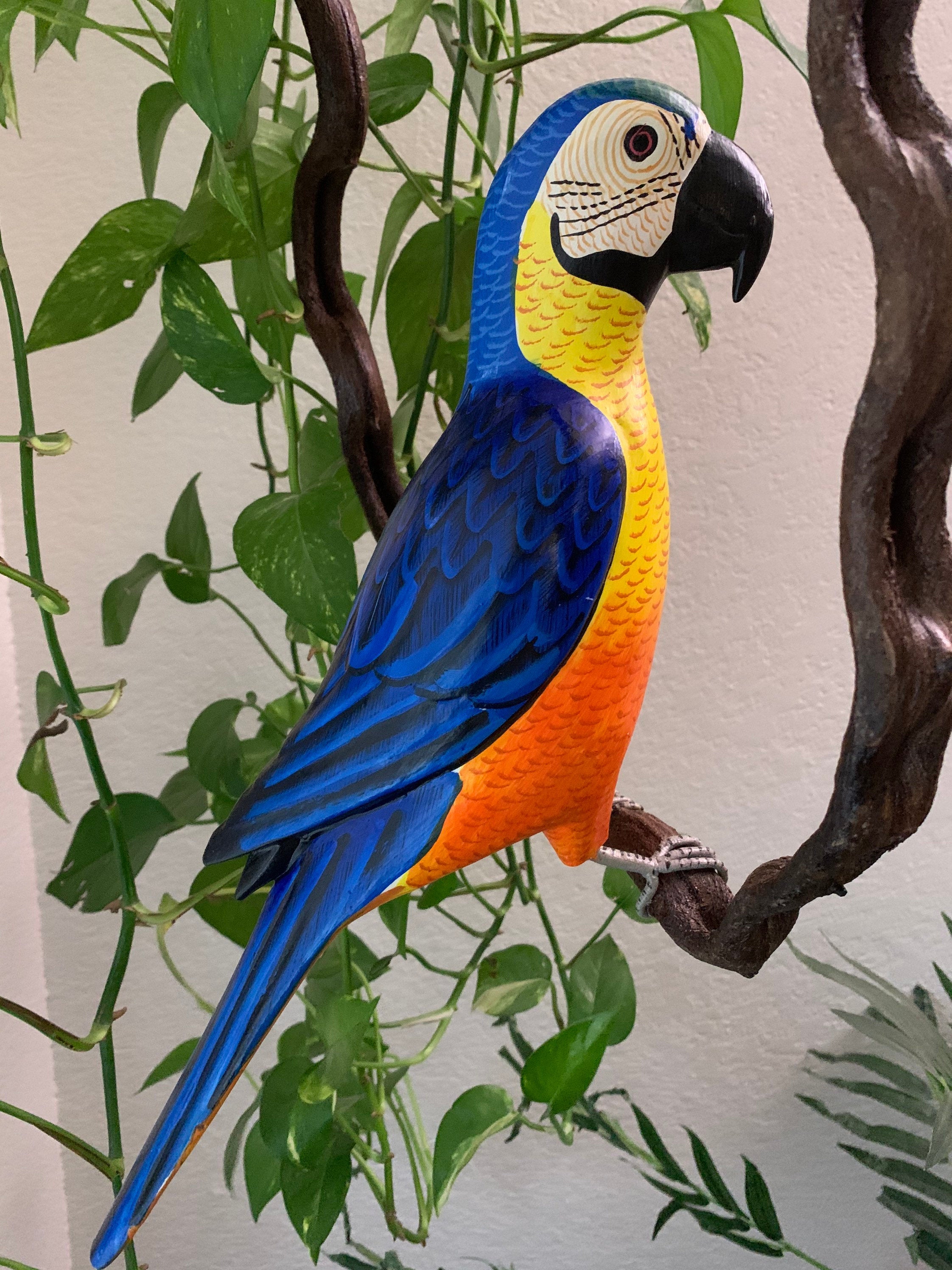 Colorful blue and yellow macaw sculpture perched on a branch among green plants