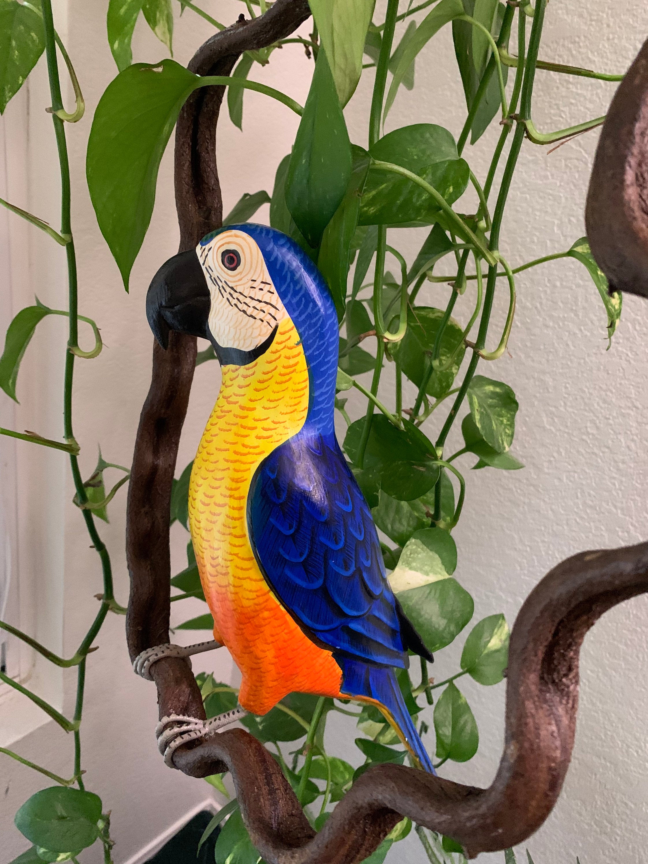 colorful blue-and-yellow parrot statue among green houseplants