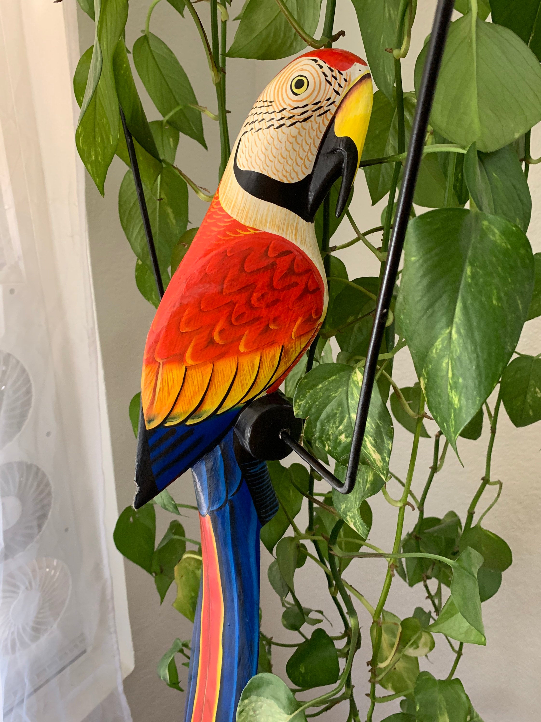 colorful carved parrot sculpture with red yellow and blue feathers among green leafy plants