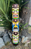 Colorful carved tiki totem pole with multiple faces and flower motifs beside a tree.