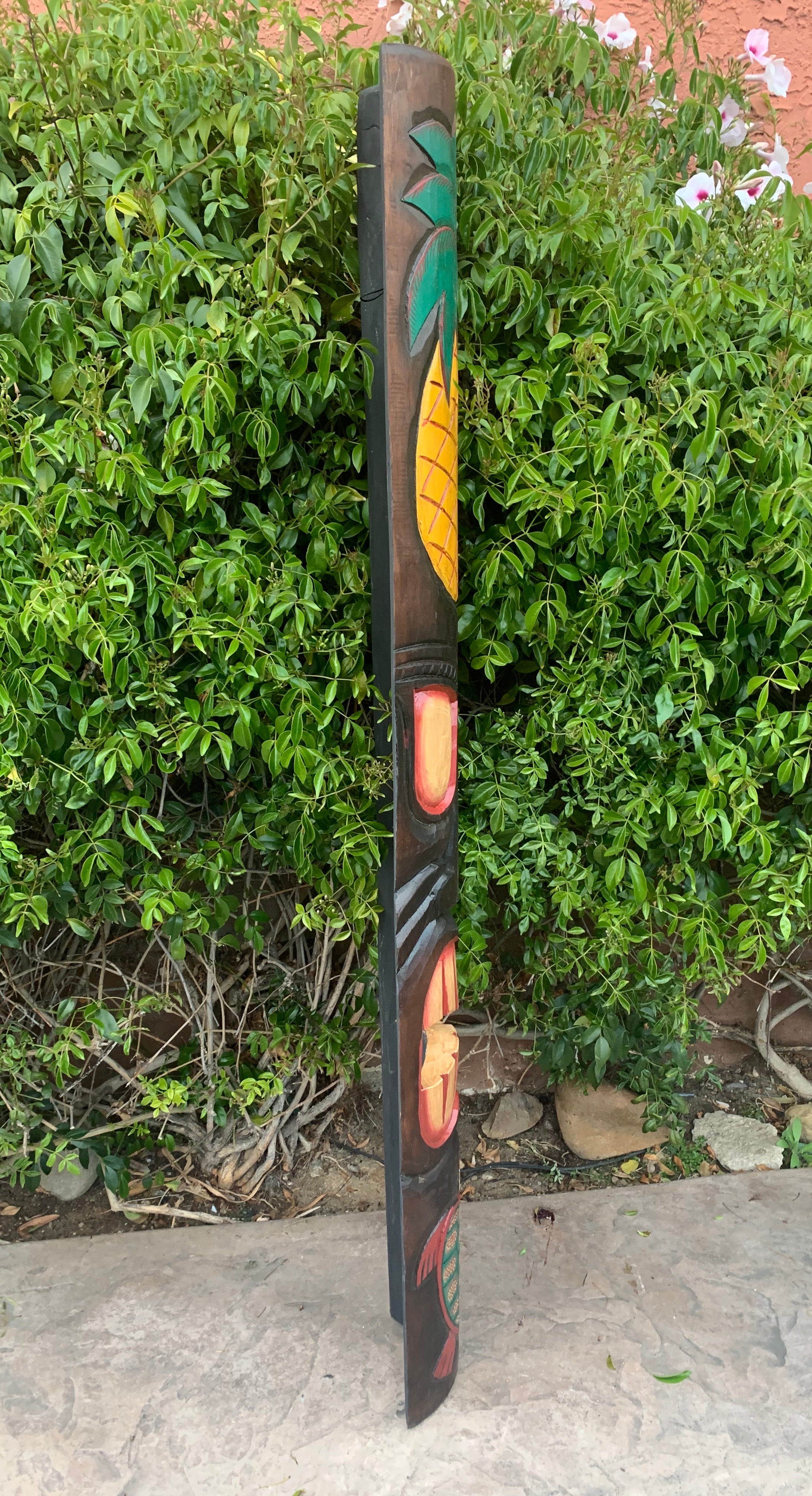 Tall carved wooden totem pole with green and yellow panels in a garden.