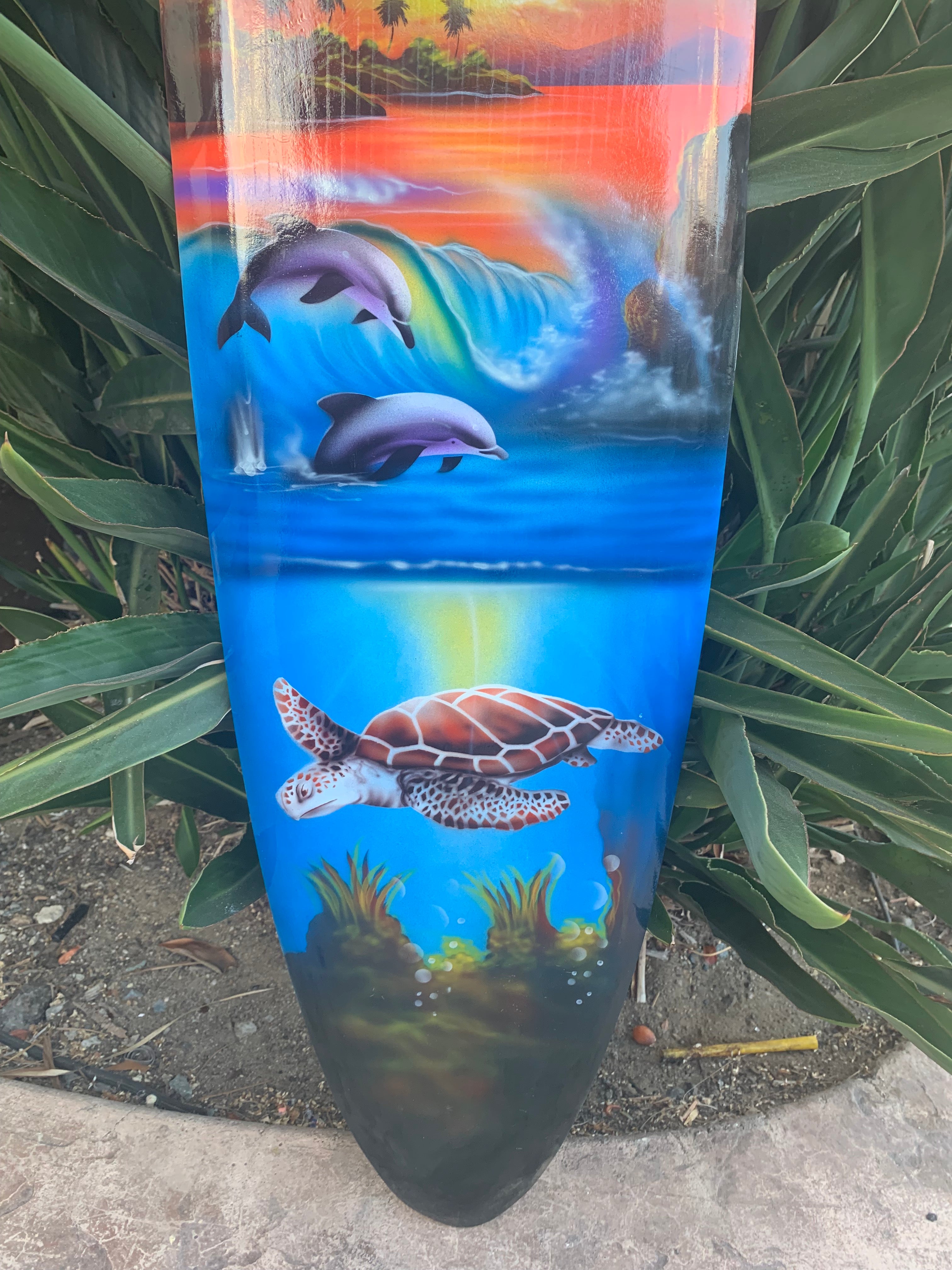 Colorful dolphins and a sea turtle painted on a surfboard with an underwater coral reef.