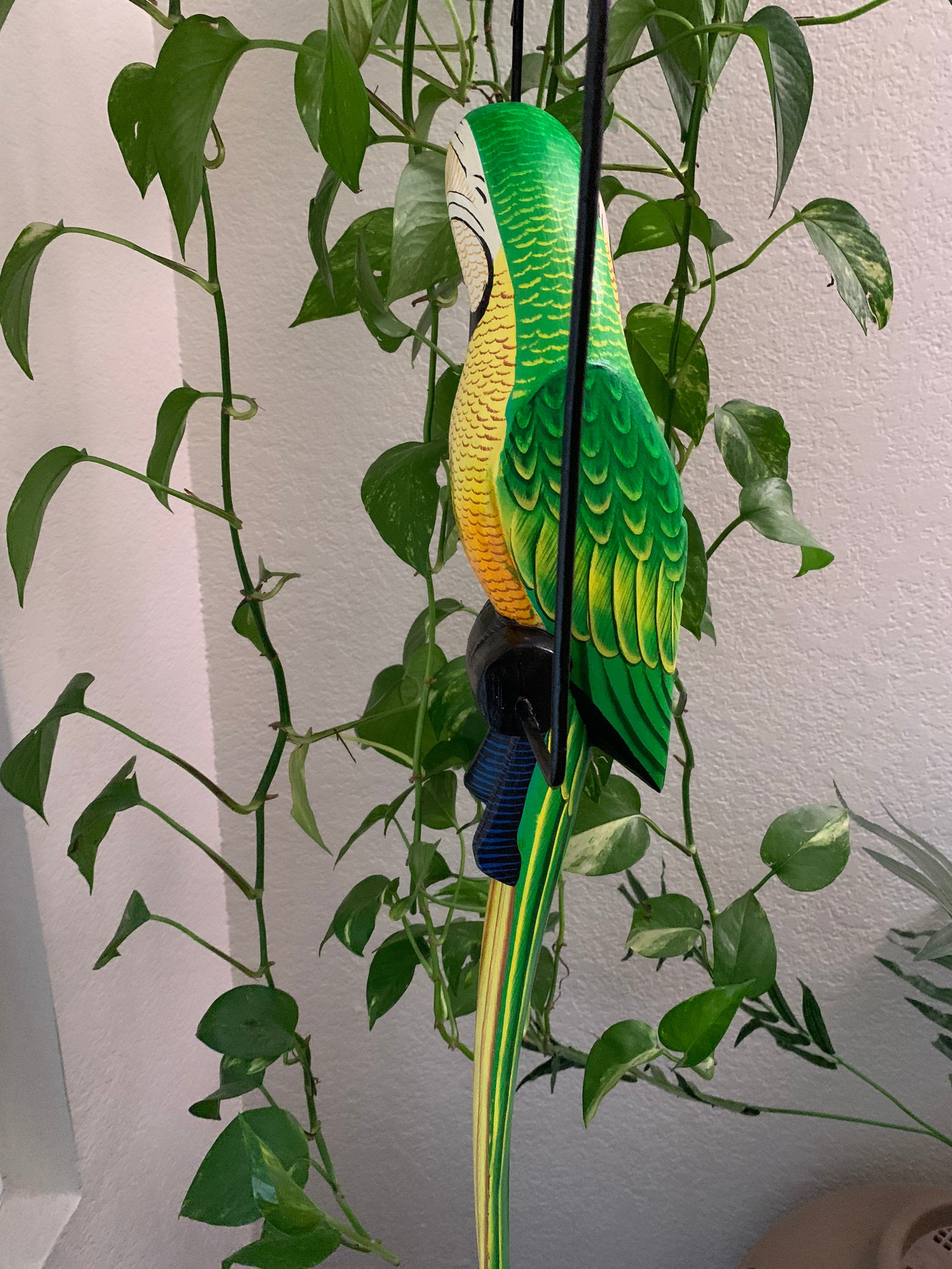 Colorful green and yellow parrot statue perched among lush houseplants.