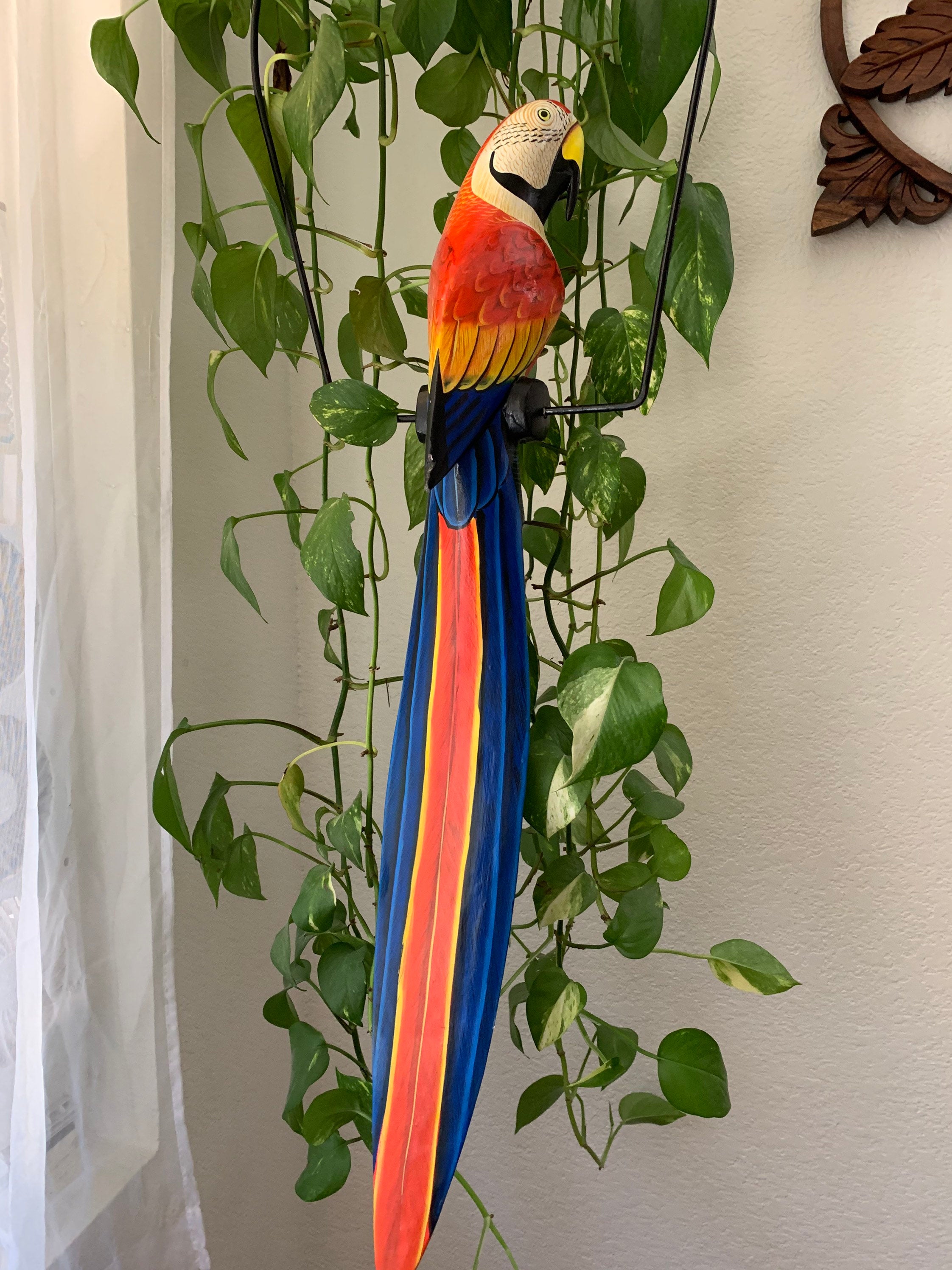 Colorful macaw parrot sculpture with a rainbow tail hanging among green plants indoors