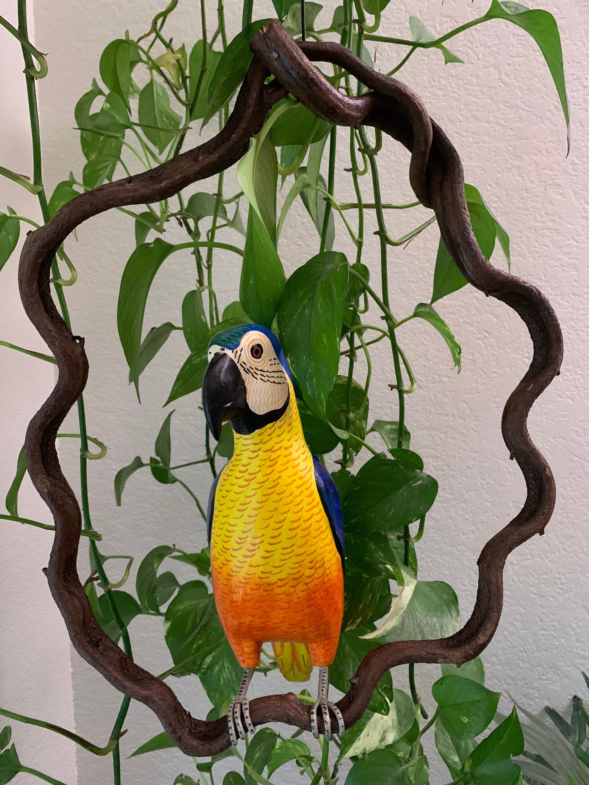 colorful macaw parrot statue perched on a curved wooden frame among green plants