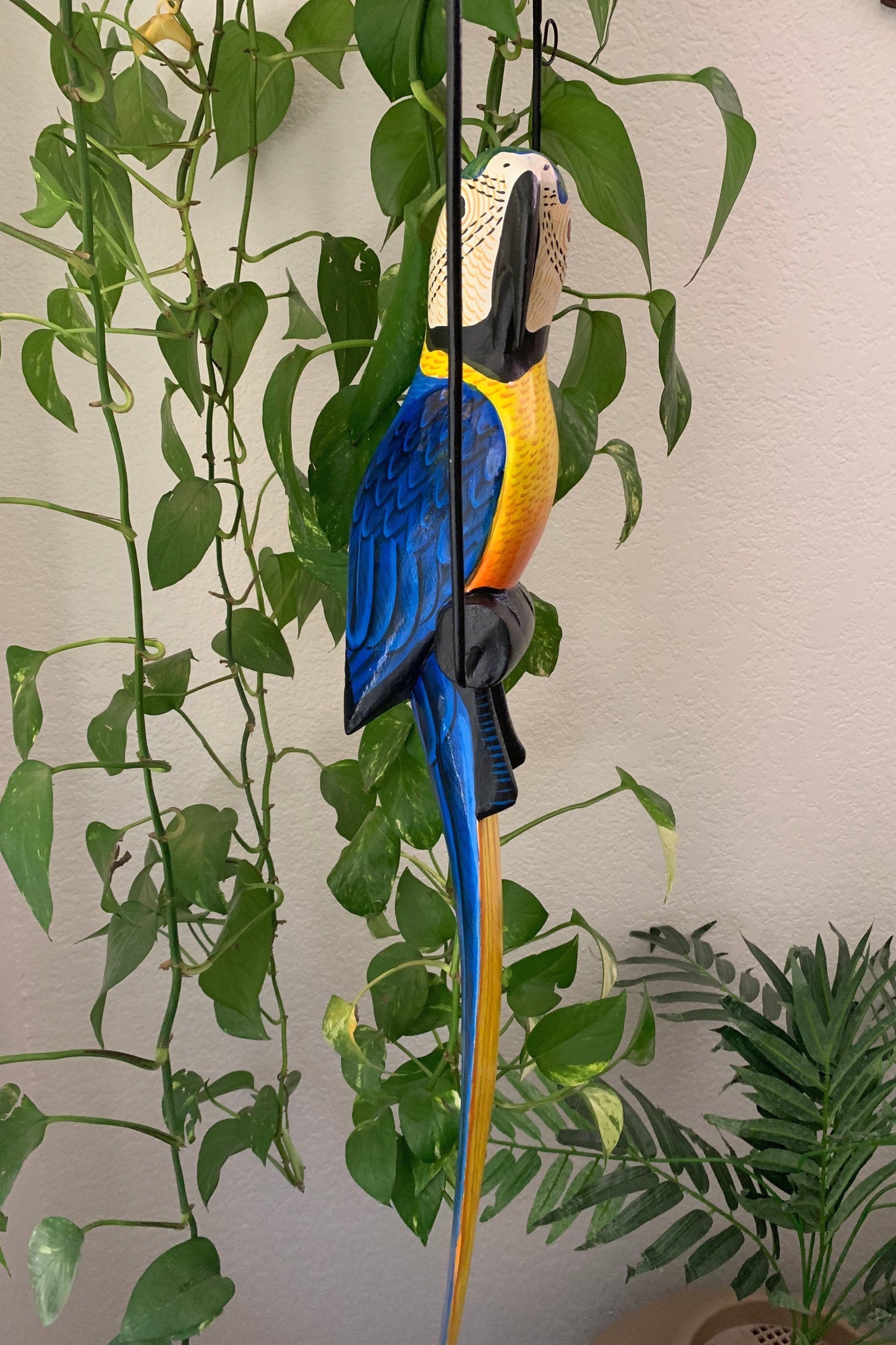 Colorful macaw sculpture hanging among green houseplants
