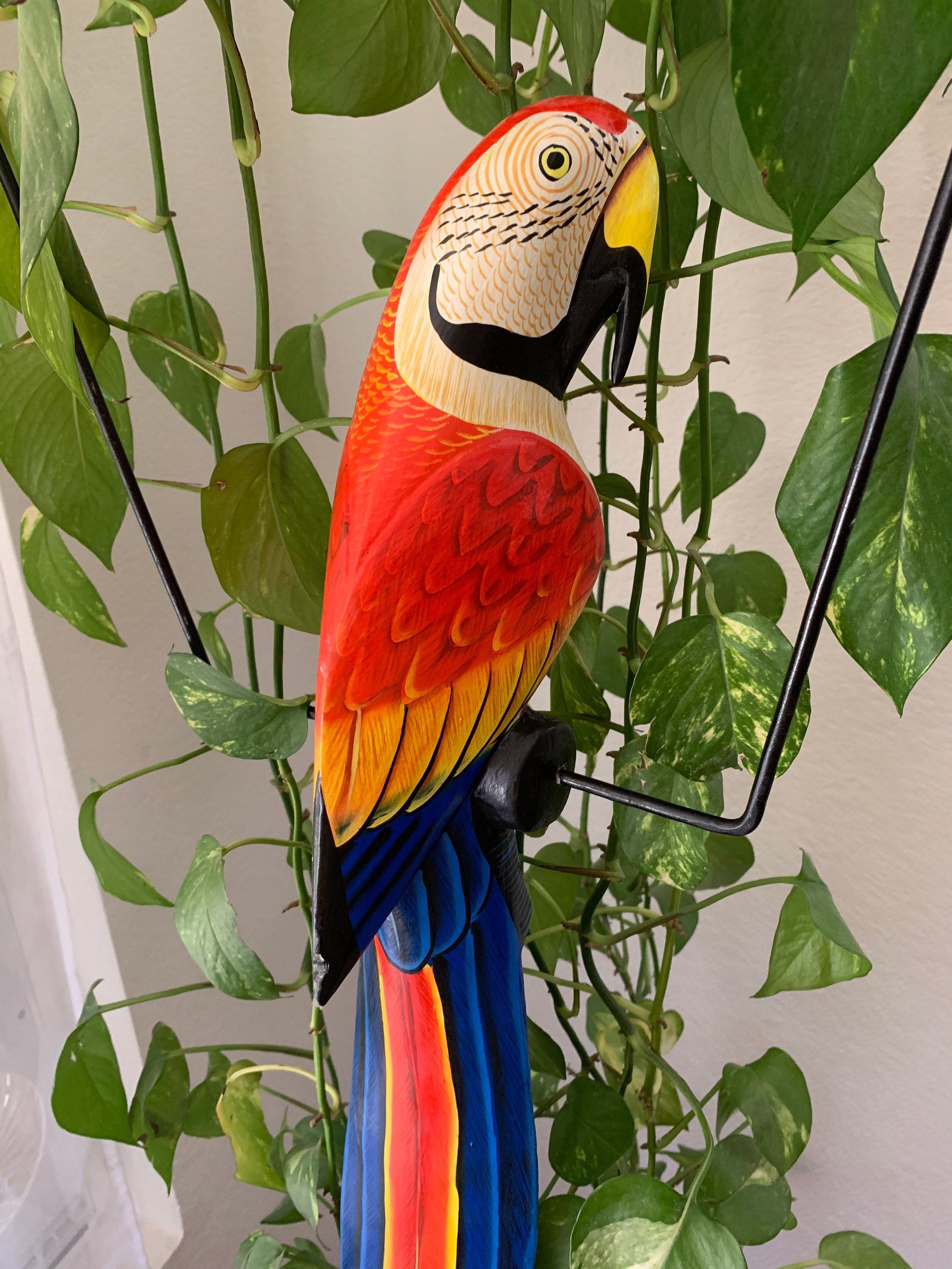 Colorful macaw sculpture perched among green houseplants