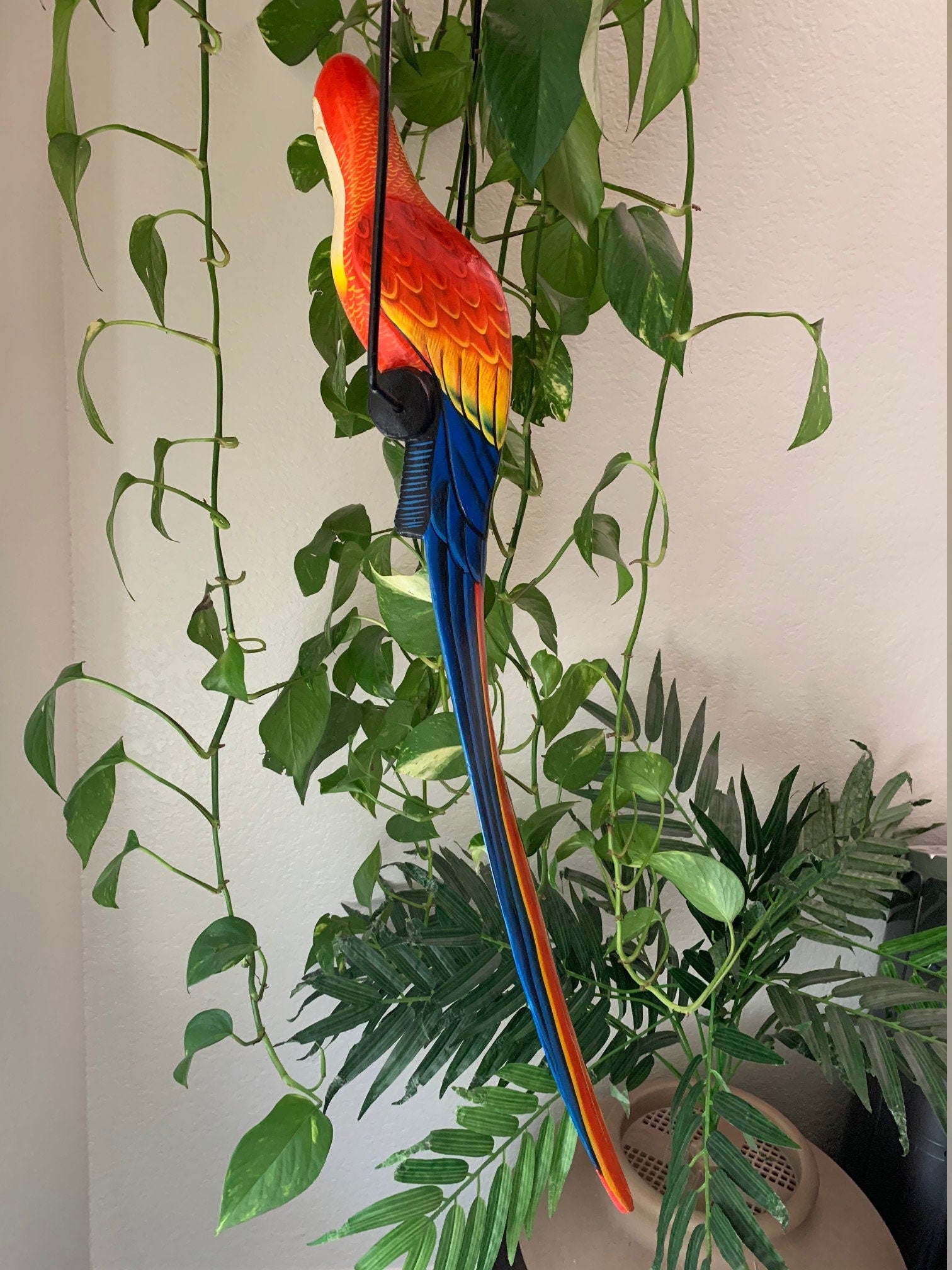 Colorful parrot decorative sculpture hanging among lush green indoor plants