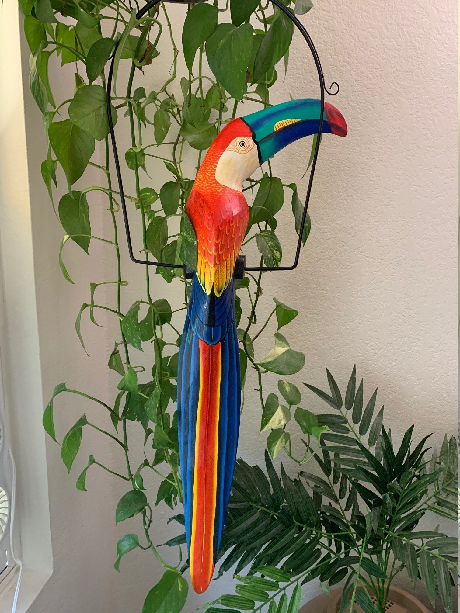 colorful rainbow toucan sculpture hanging among green houseplants
