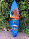 Colorful surfboard featuring tropical sunset, palm trees, dolphins and sea turtles against blue ocean.