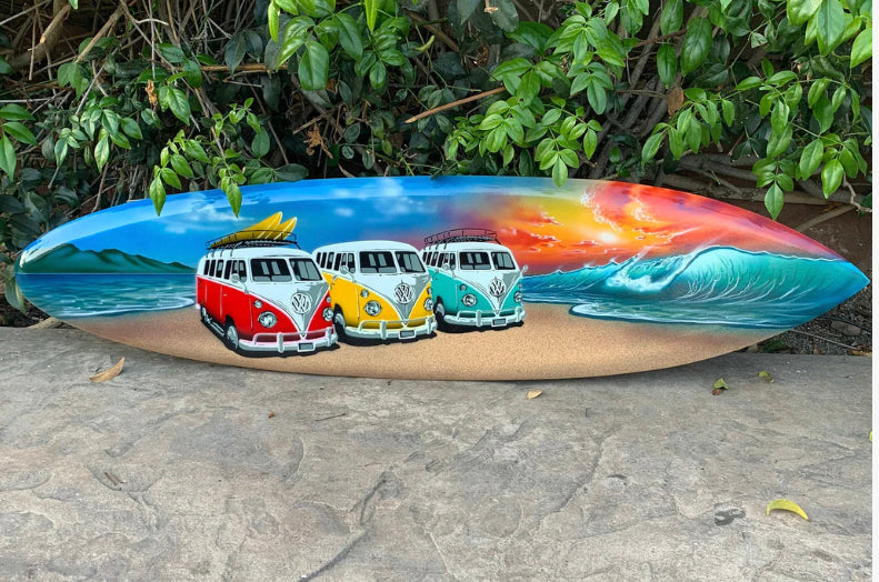 Colorful surfboard painted with red, yellow and teal VW camper vans on a beach at sunset